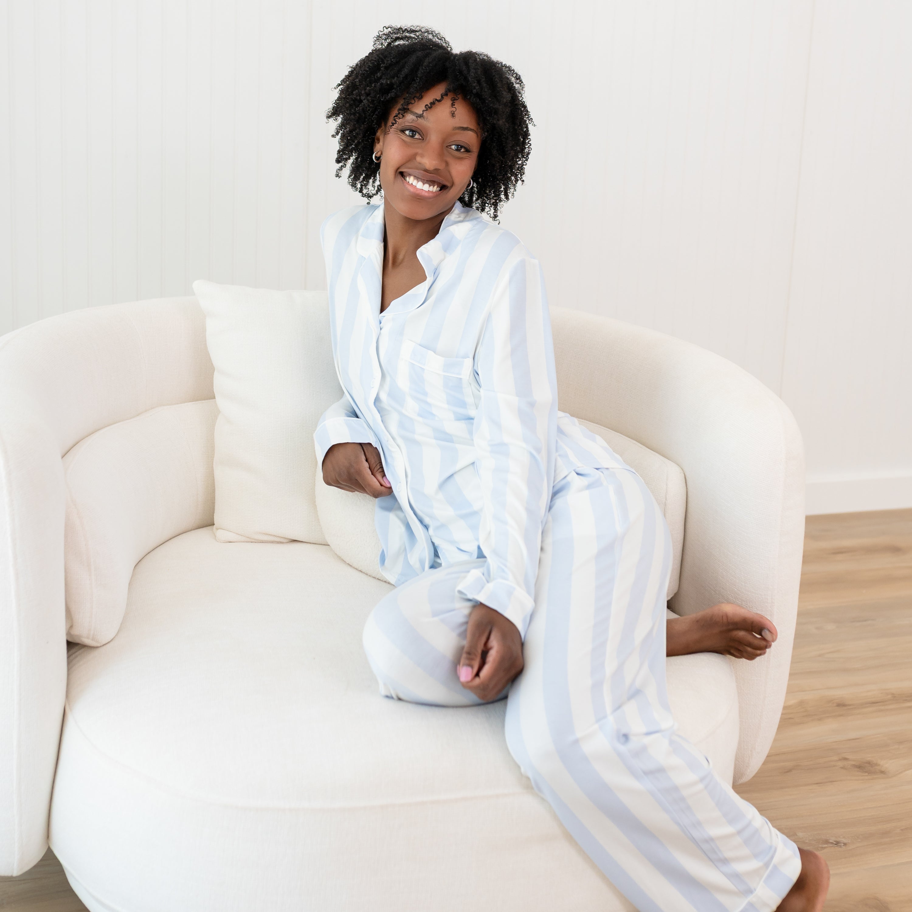 Smiling female model wearing the Long-Sleeved Women's Pajama Set in Big Mist Stripe while sitting on a cream colored couch