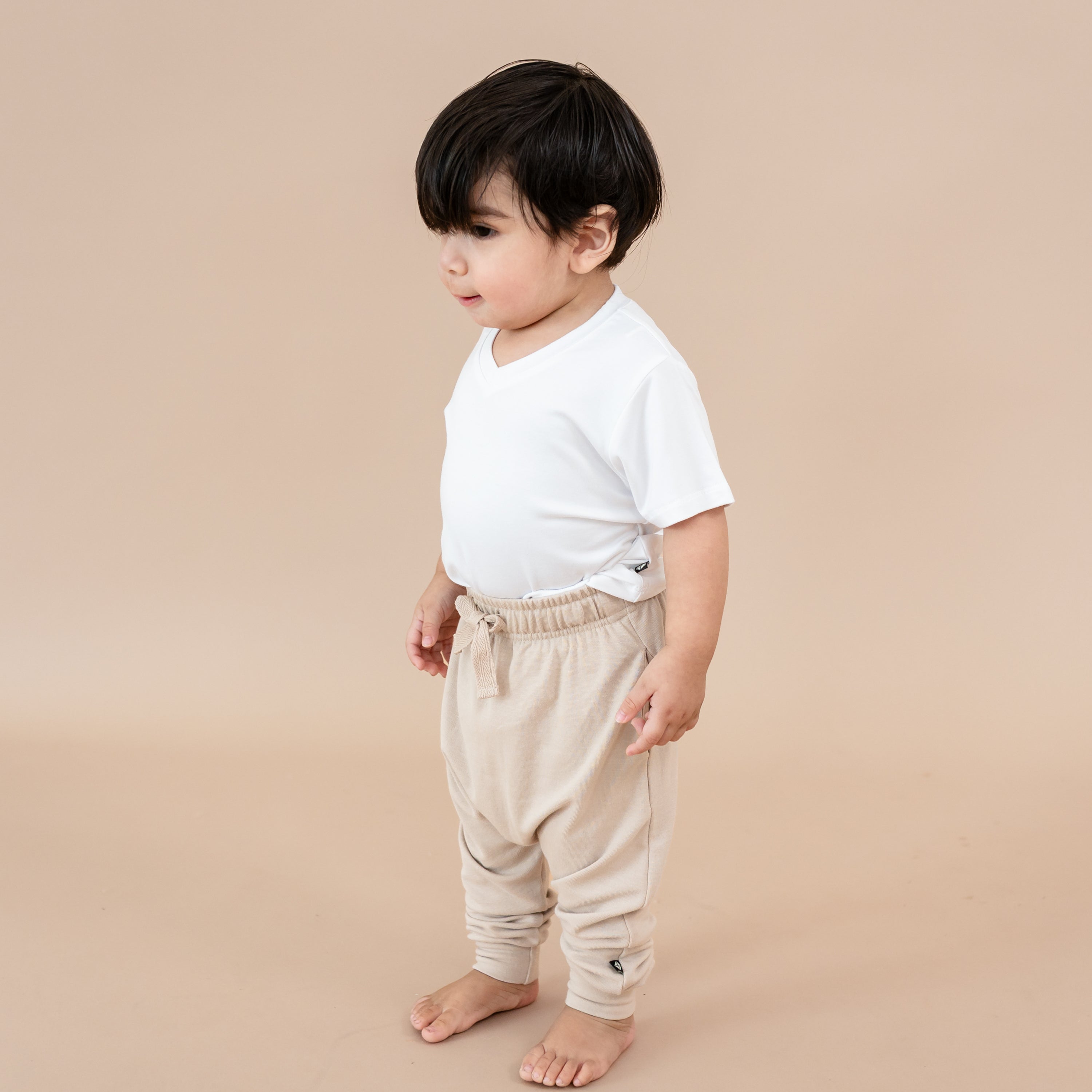 Toddler standing in front of a taupe background wearing the Bamboo Jersey Harem Pants in Bisque paired with a toddler v-neck in snow