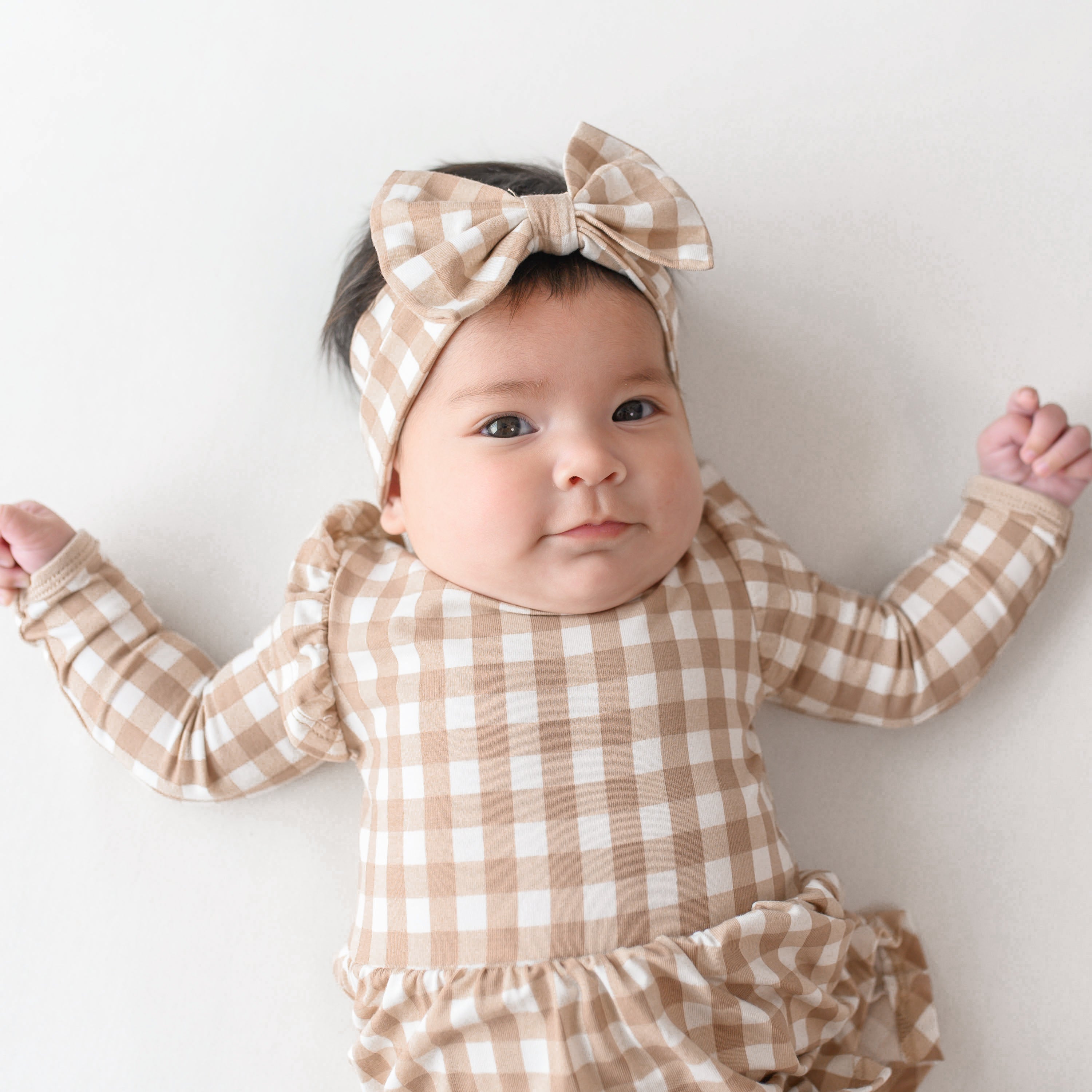 Infant wearing Bow Headband and Long Sleeve Twirl Bodysuit Dress in Gingham Bisque