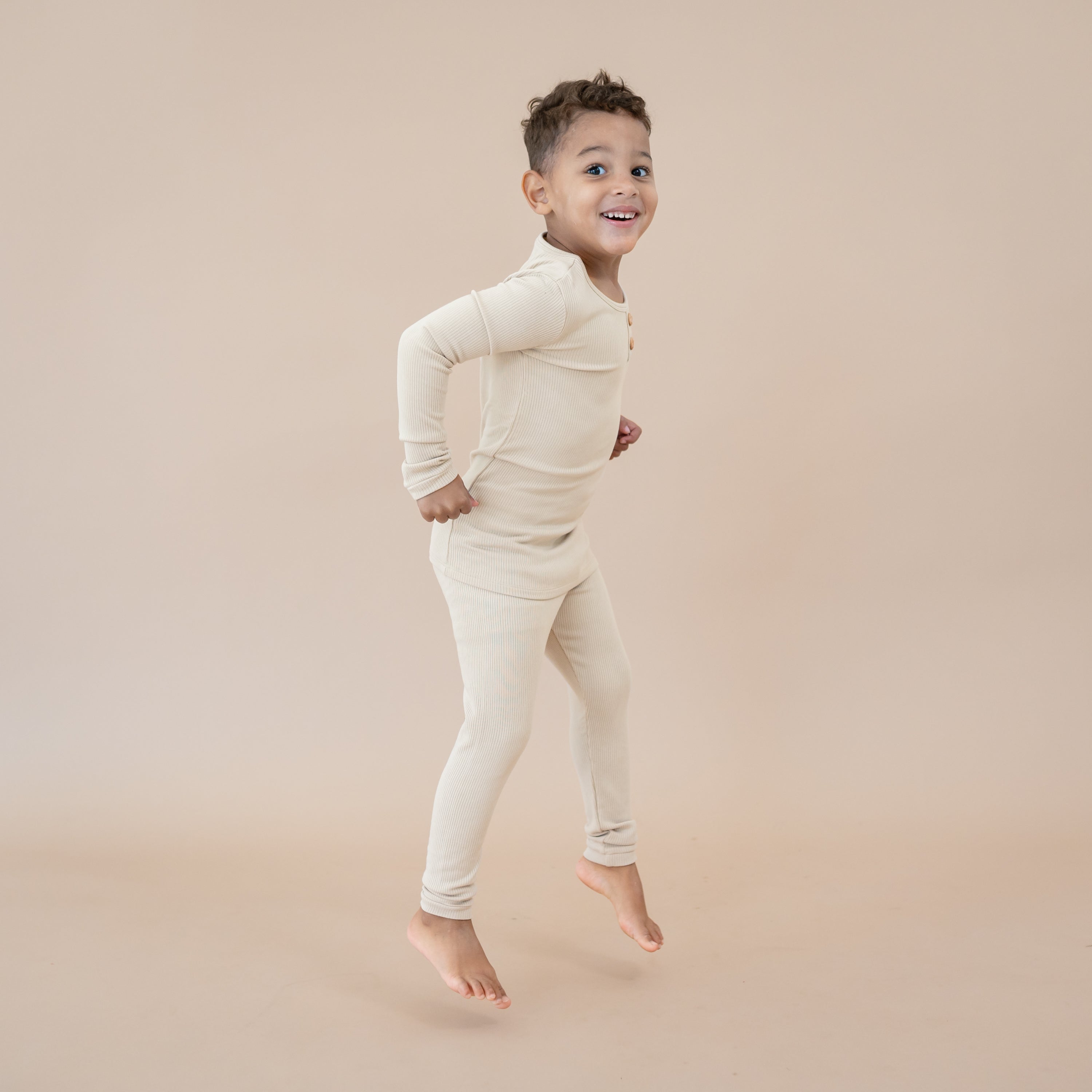 Young boy jumping in the Ribbed Henley Set in Bisque showing the side view of the set