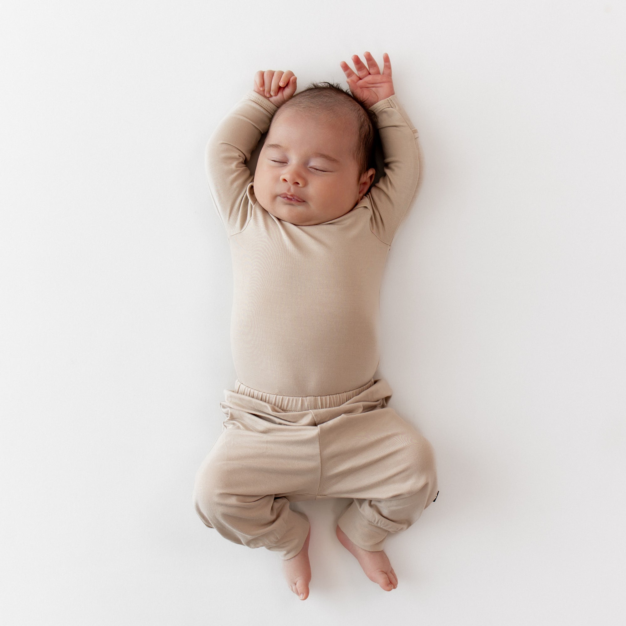 Sleeping newborn wearing the Pant in Bisque paired with a matching long sleeve bodysuit