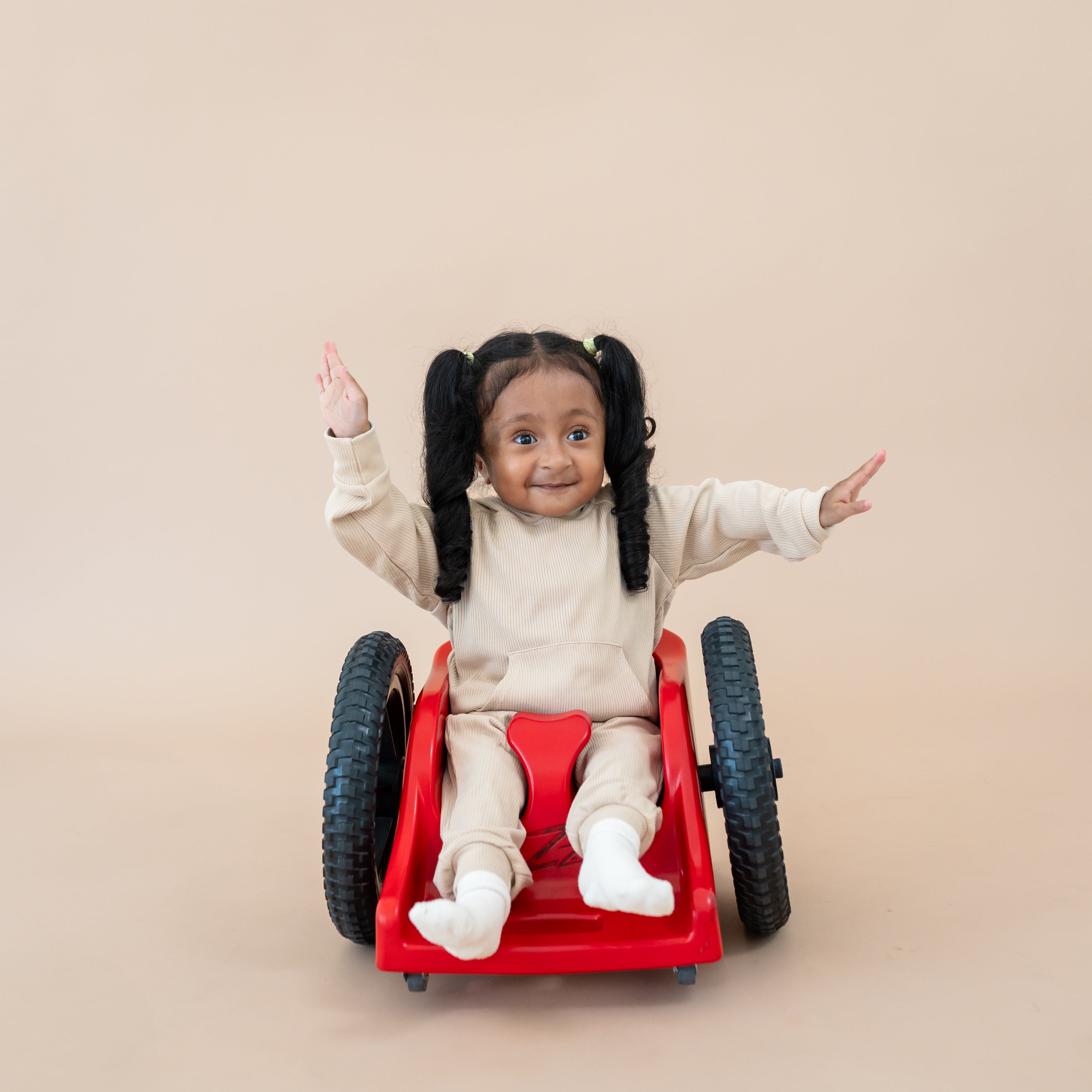 Toddler girl sitting in her wheel chair with hands in the air wearing the Ribbed Jogger Pant in Bisque and matching Ribbed Bisque hoodie