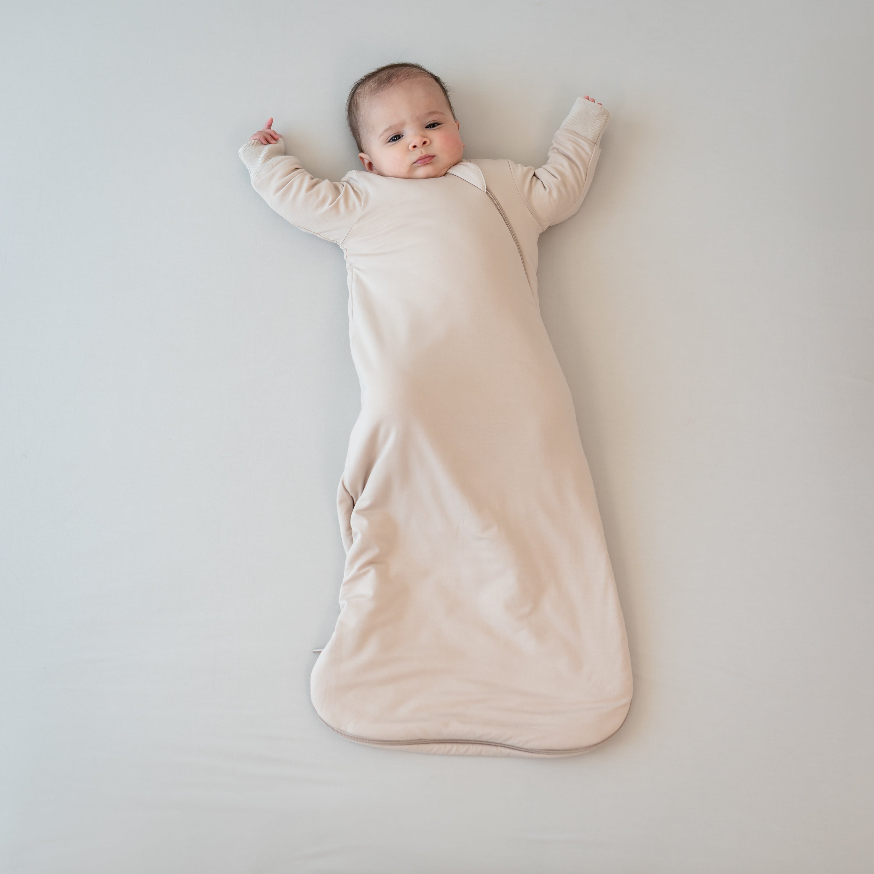 Infant laying down with hands up wearing the Slumber Bag in Bisque