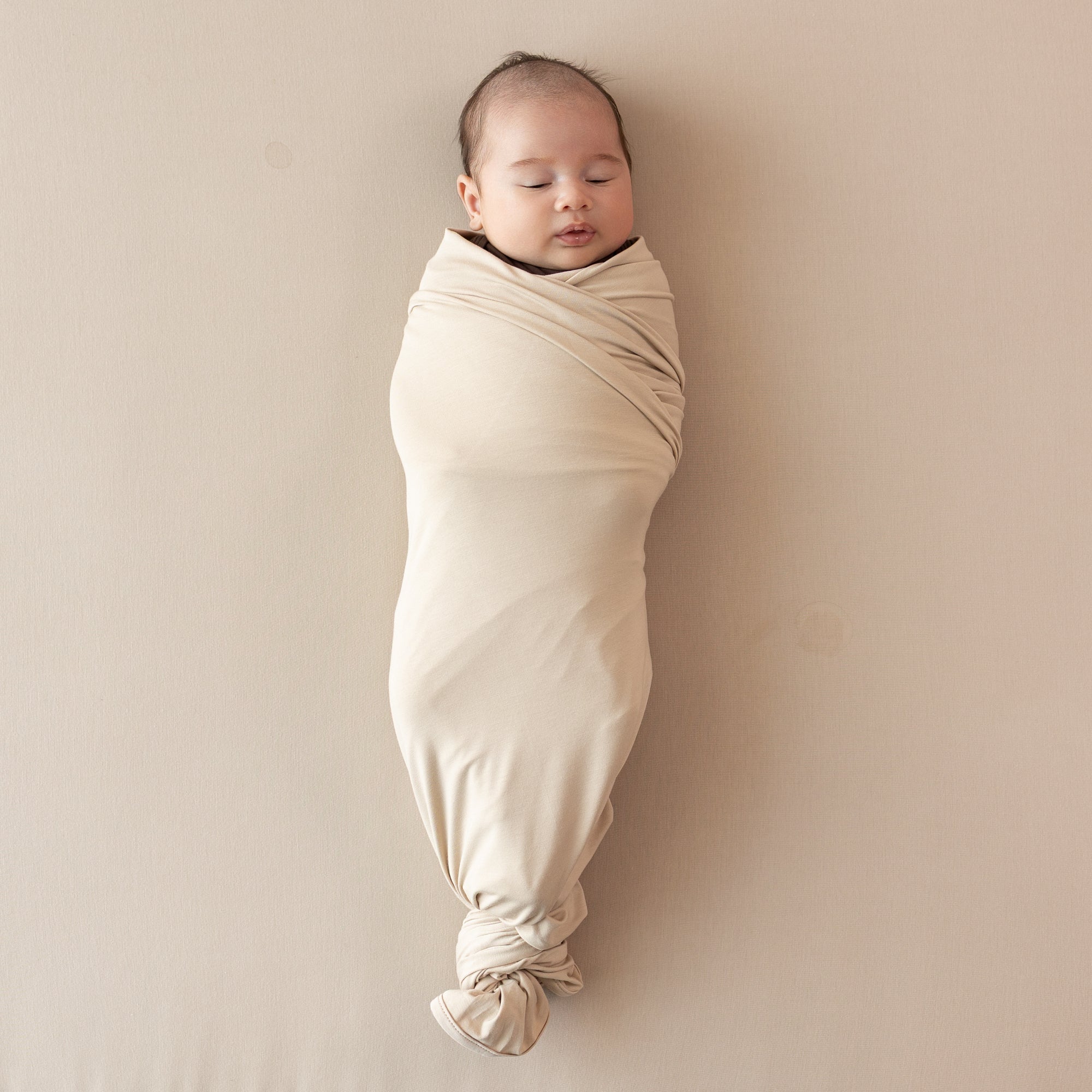 Sleeping infant swaddled in the Swaddle Blanket in Bisque