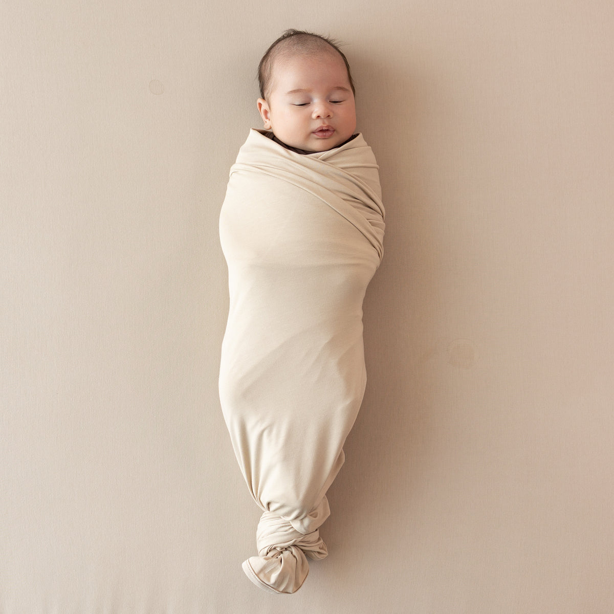 Sleeping infant swaddled in the Swaddle Blanket in Bisque