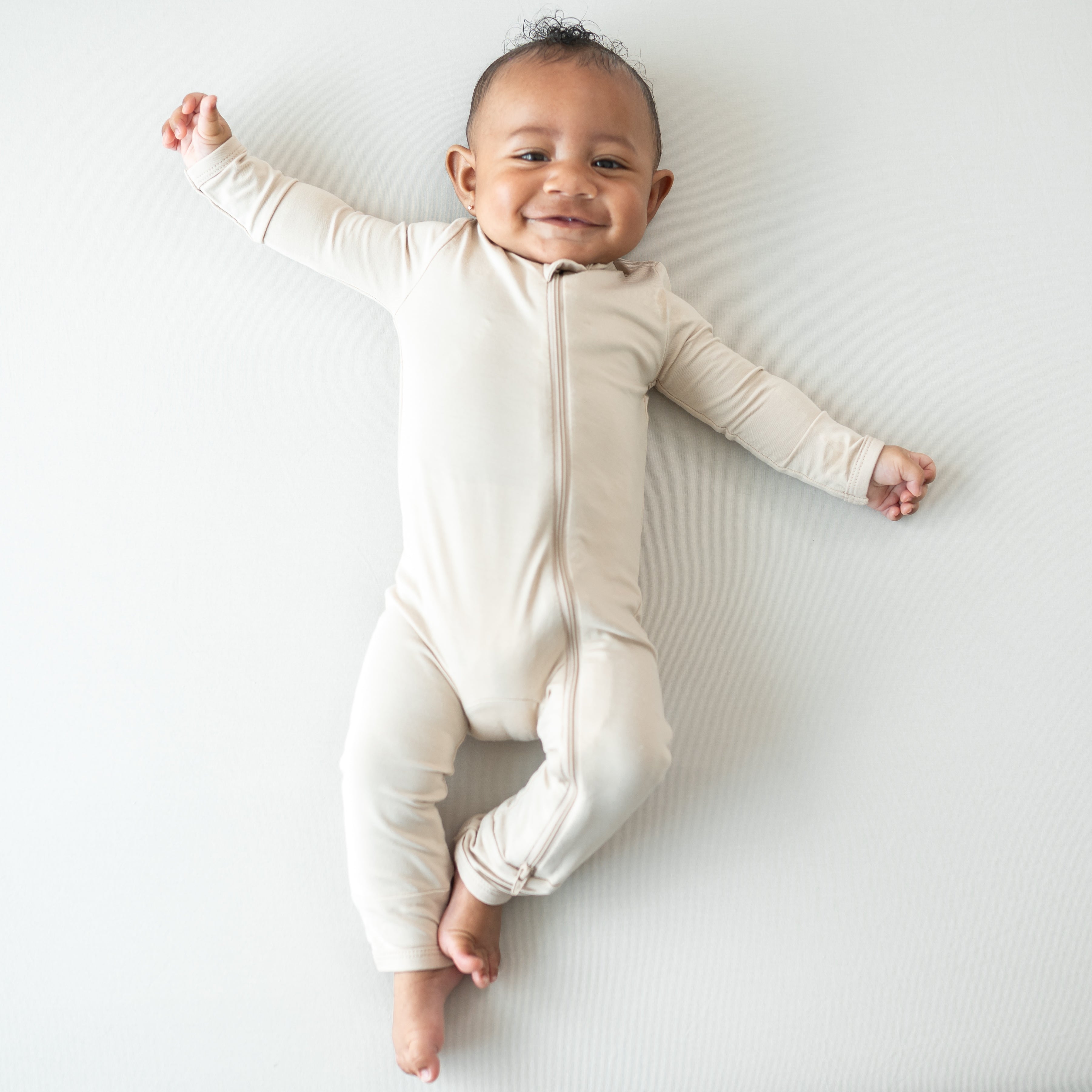 Smiling infant wearing the Zippered Romper in Bisque