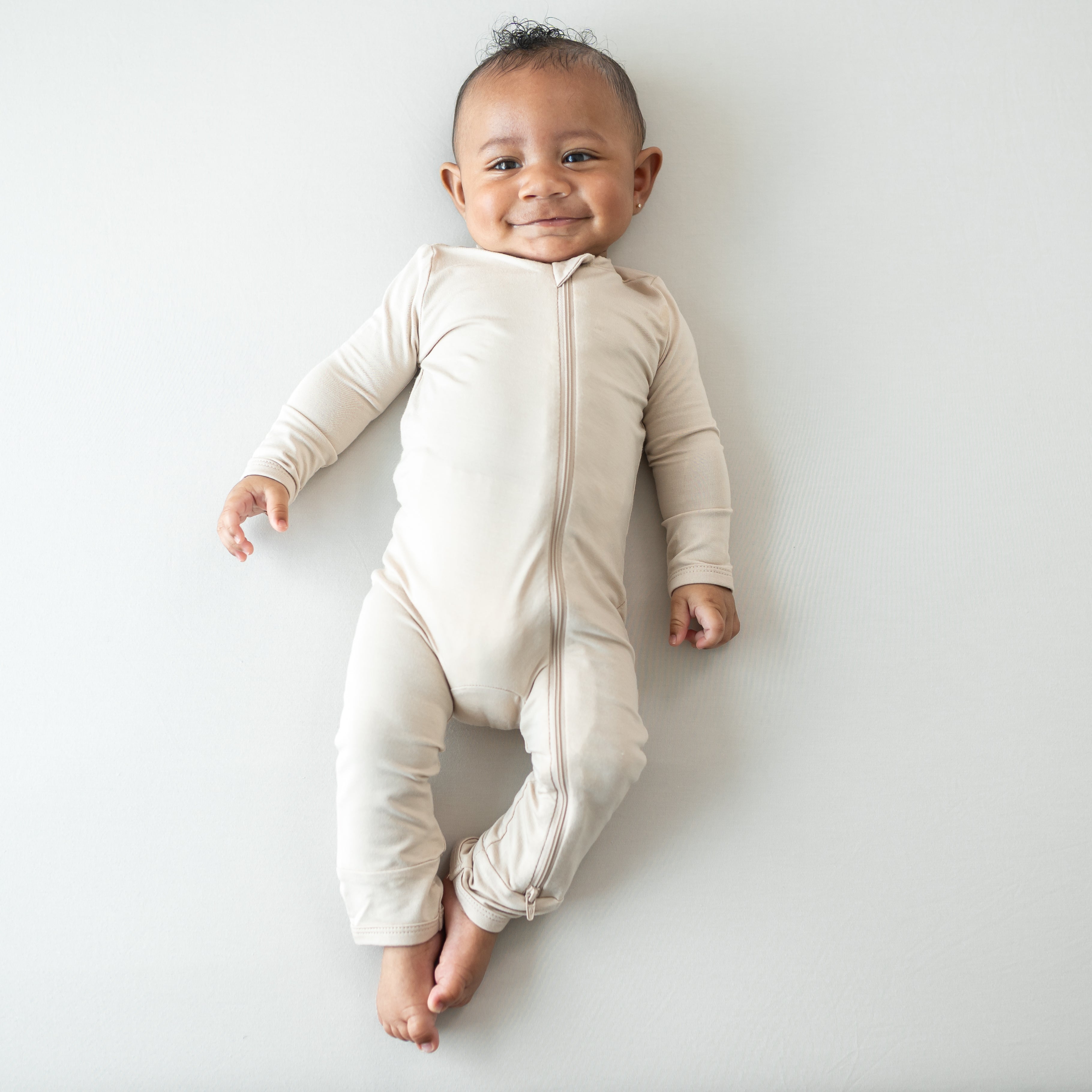 Smiling infant wearing the Zippered Romper in Bisque