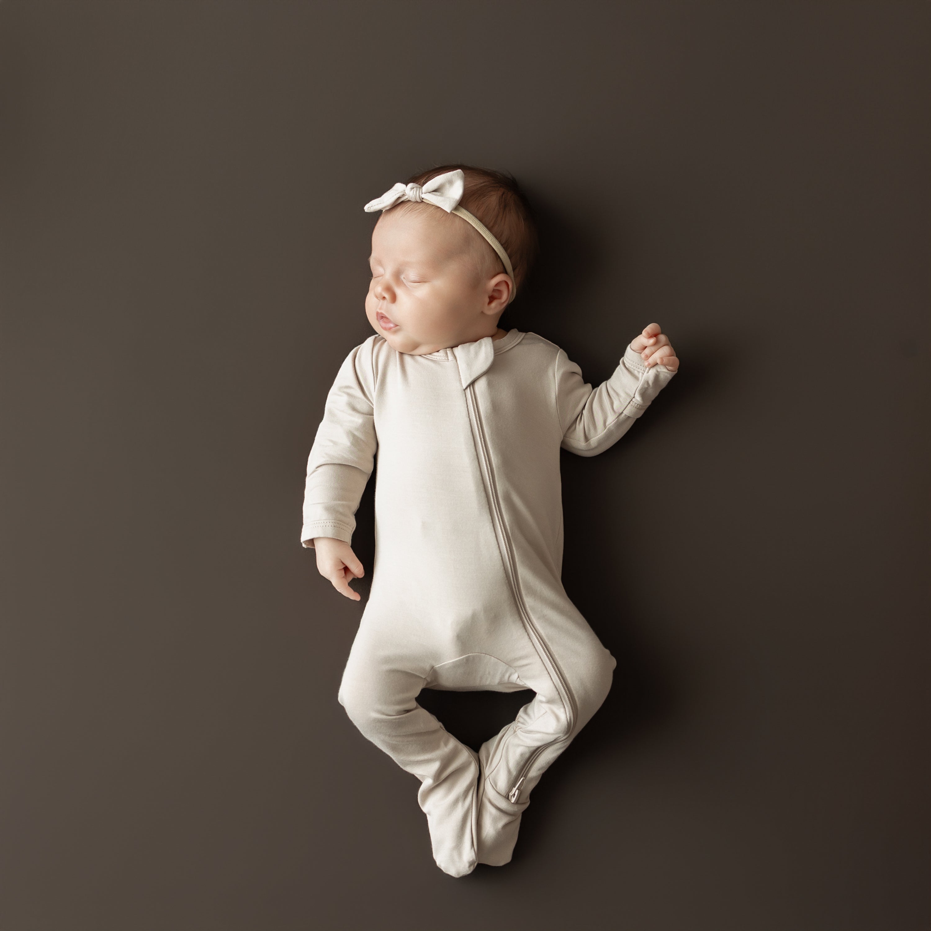 Sleeping infant wearing the Zippered Footie in Bisque with matching Tiny Nylon Bow