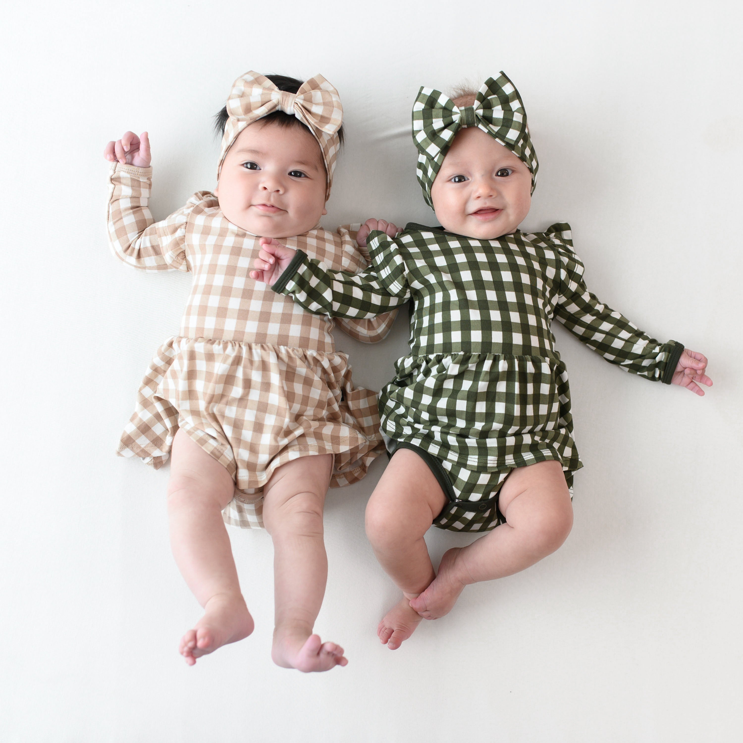 Two infants wearing Bow Headbands and Long Sleeve Twirl Dresses in Christmas Gingham prints