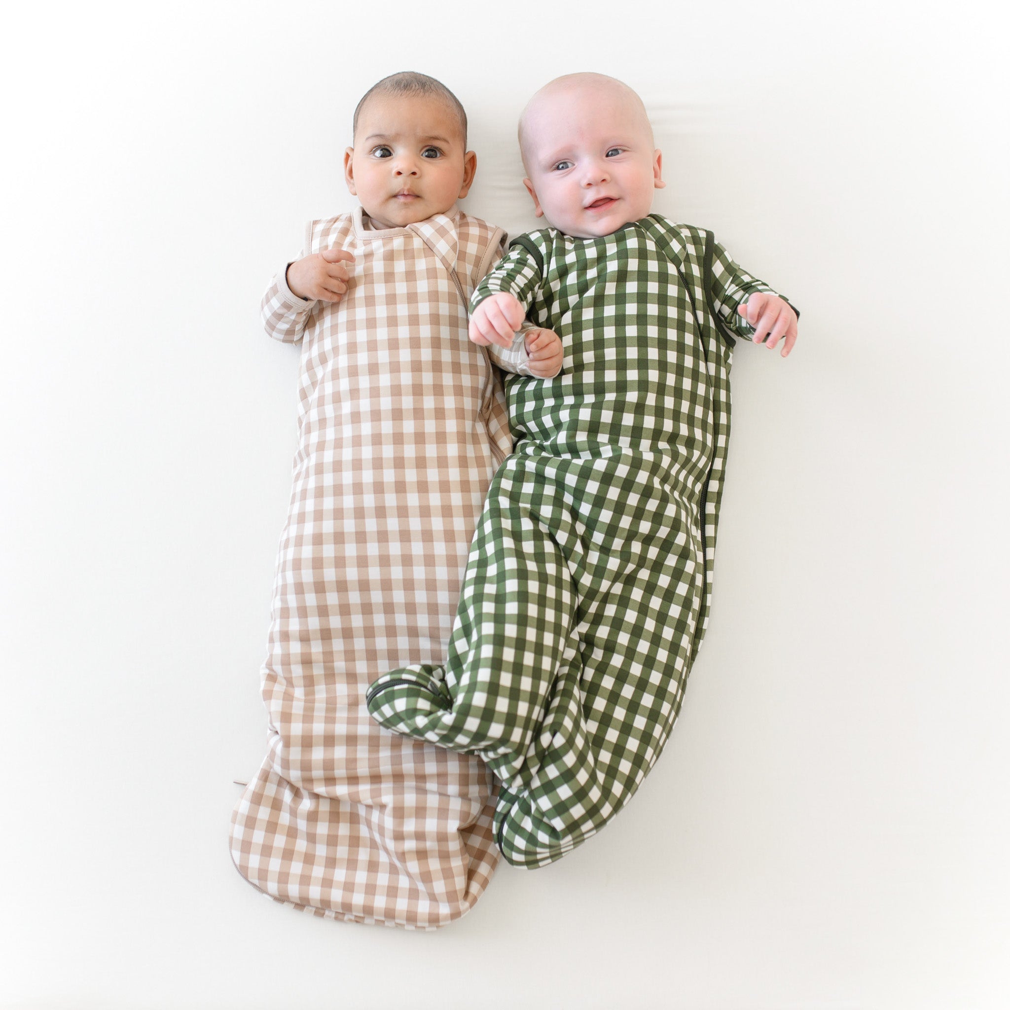 Two infants wearing TOG 1.0 Sleep Bag in Gingham Fir and Gingham Bisque over matching long sleeve rompers