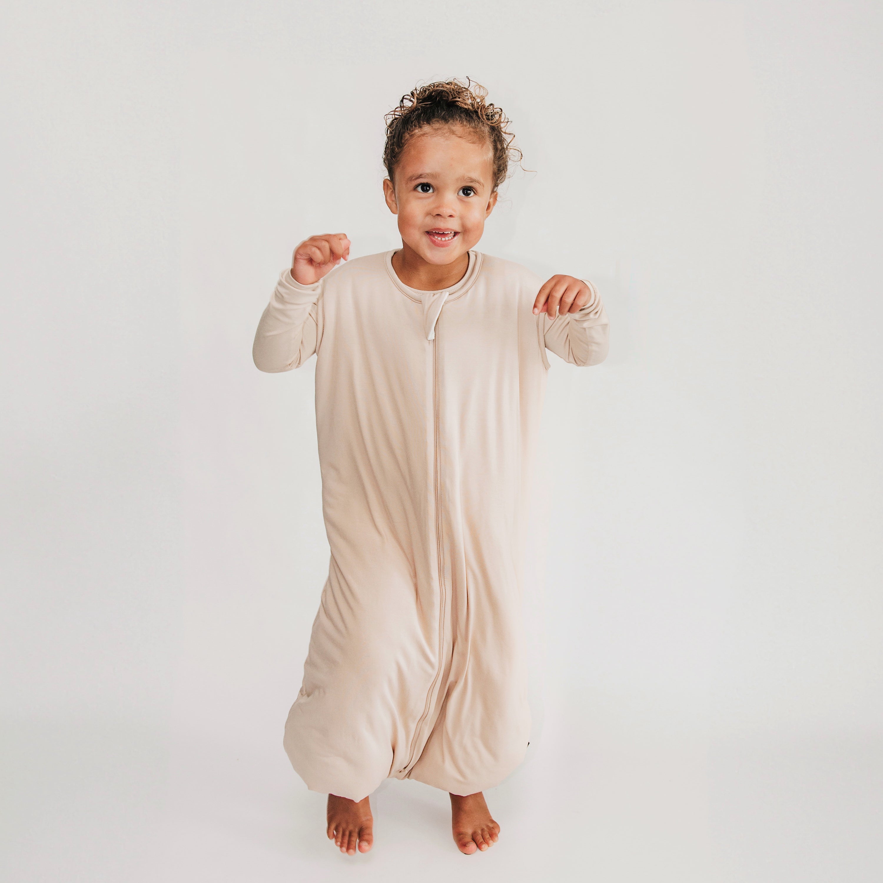 Young kid jumping wearing the Sleep Bag Walker in Bisque 2.5 and matching long sleeve toddler pajamas on underneath