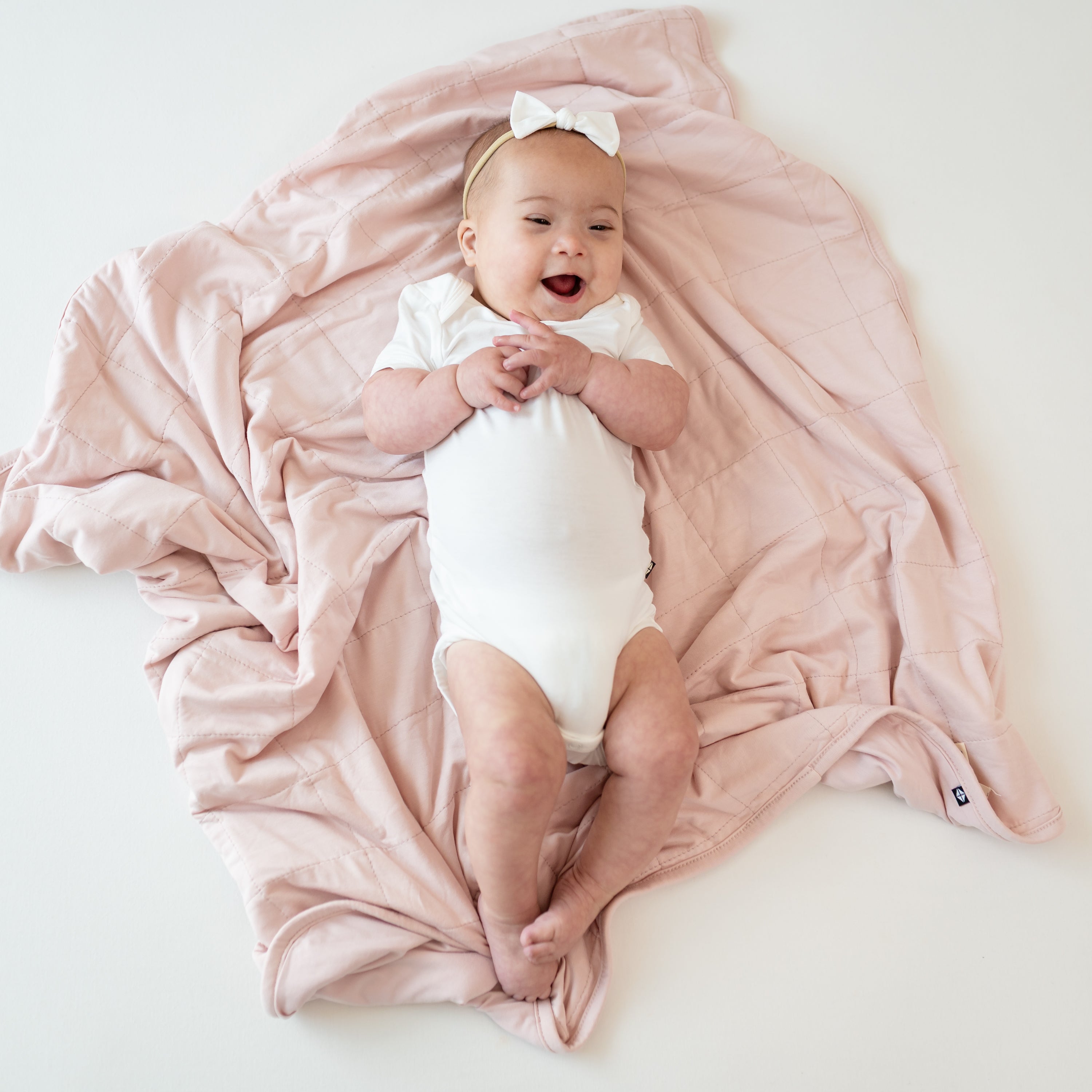 Baby wearing a Cloud Bodysuit laying on Baby Blanket in Blush 1.0
