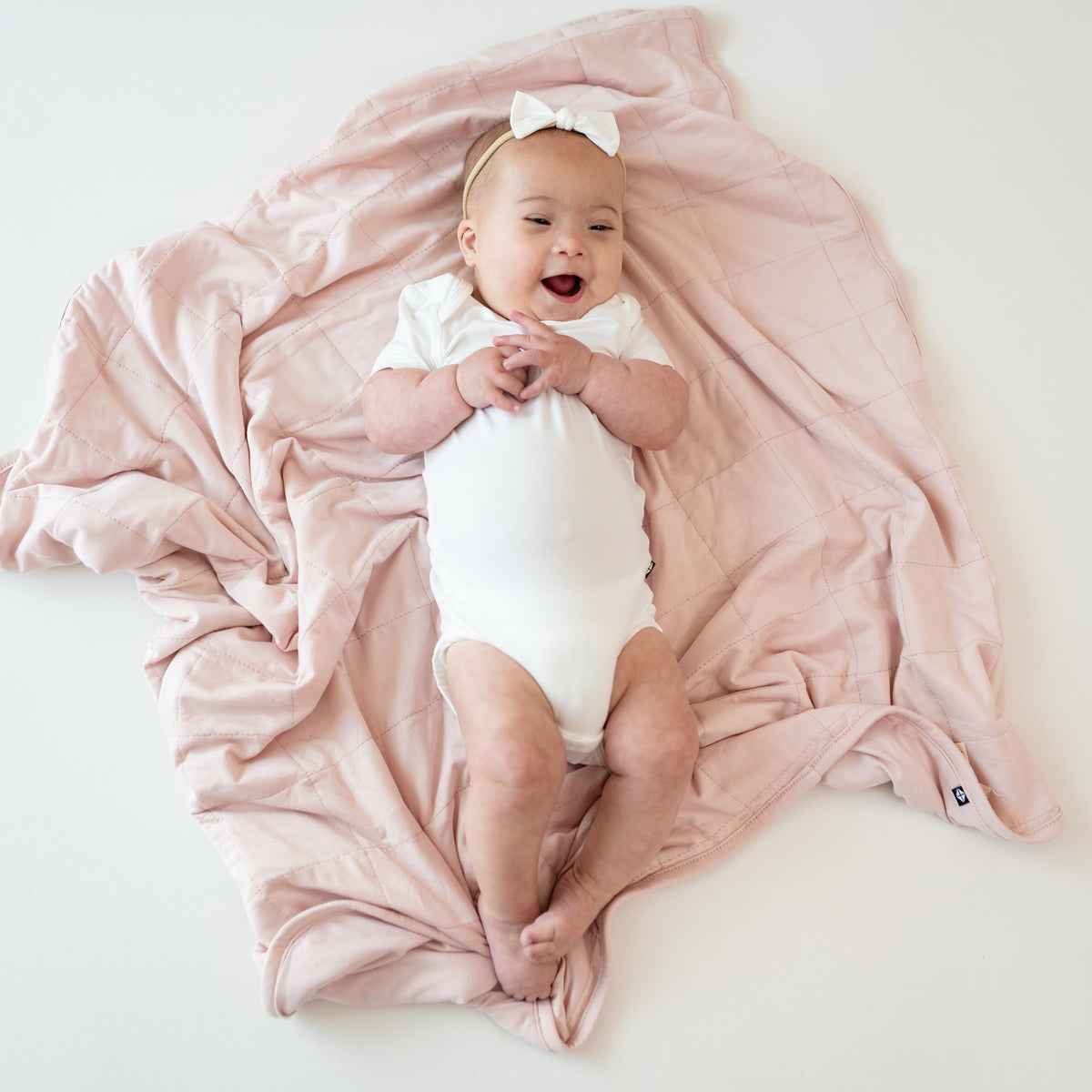 Baby wearing a Cloud Bodysuit laying on Baby Blanket in Blush 1.0