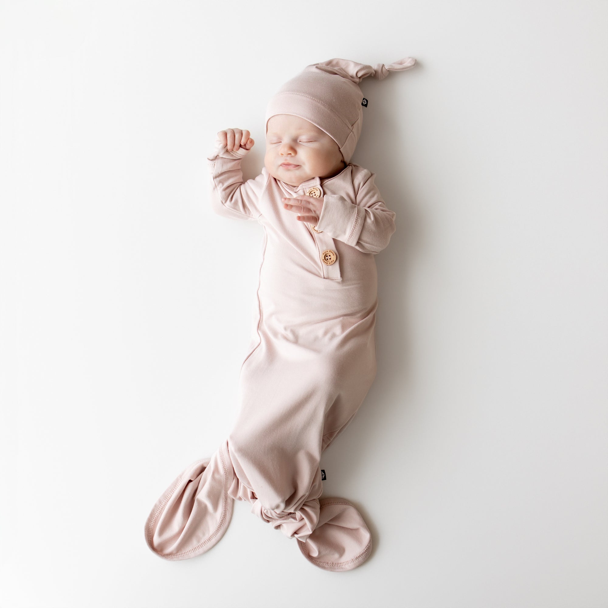 Newborn baby in a pink knotted gown and hat on a white background