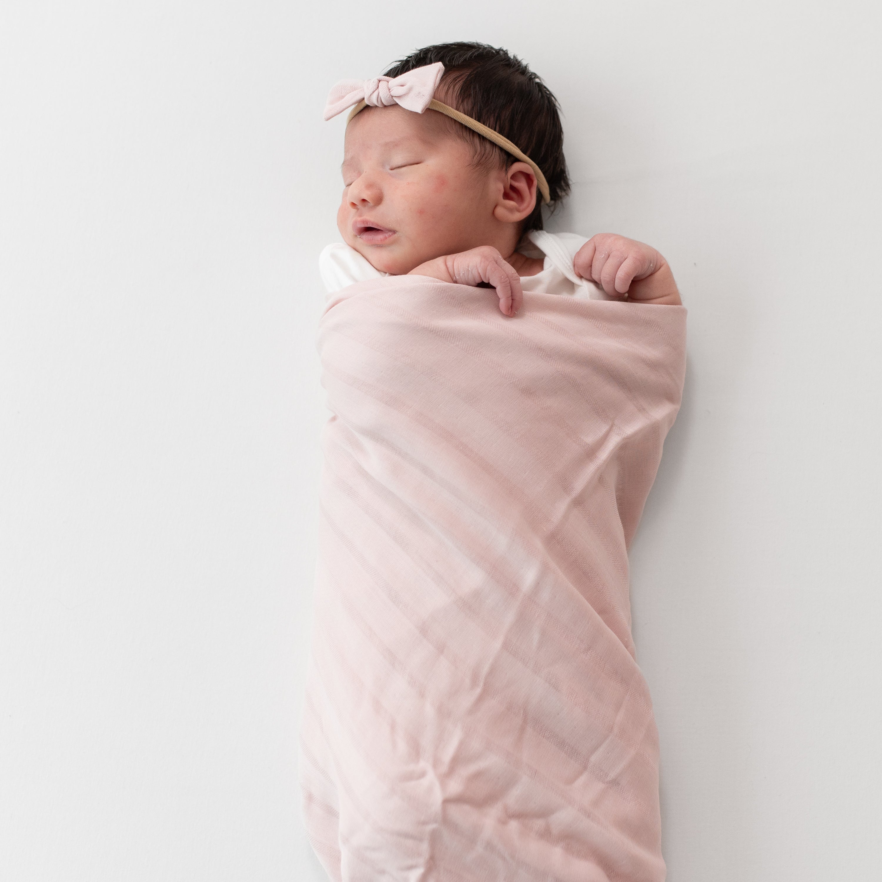Baby wrapped in Blush Pink Bamboo Muslin Swaddle Blanket with Woven Stripe Detail