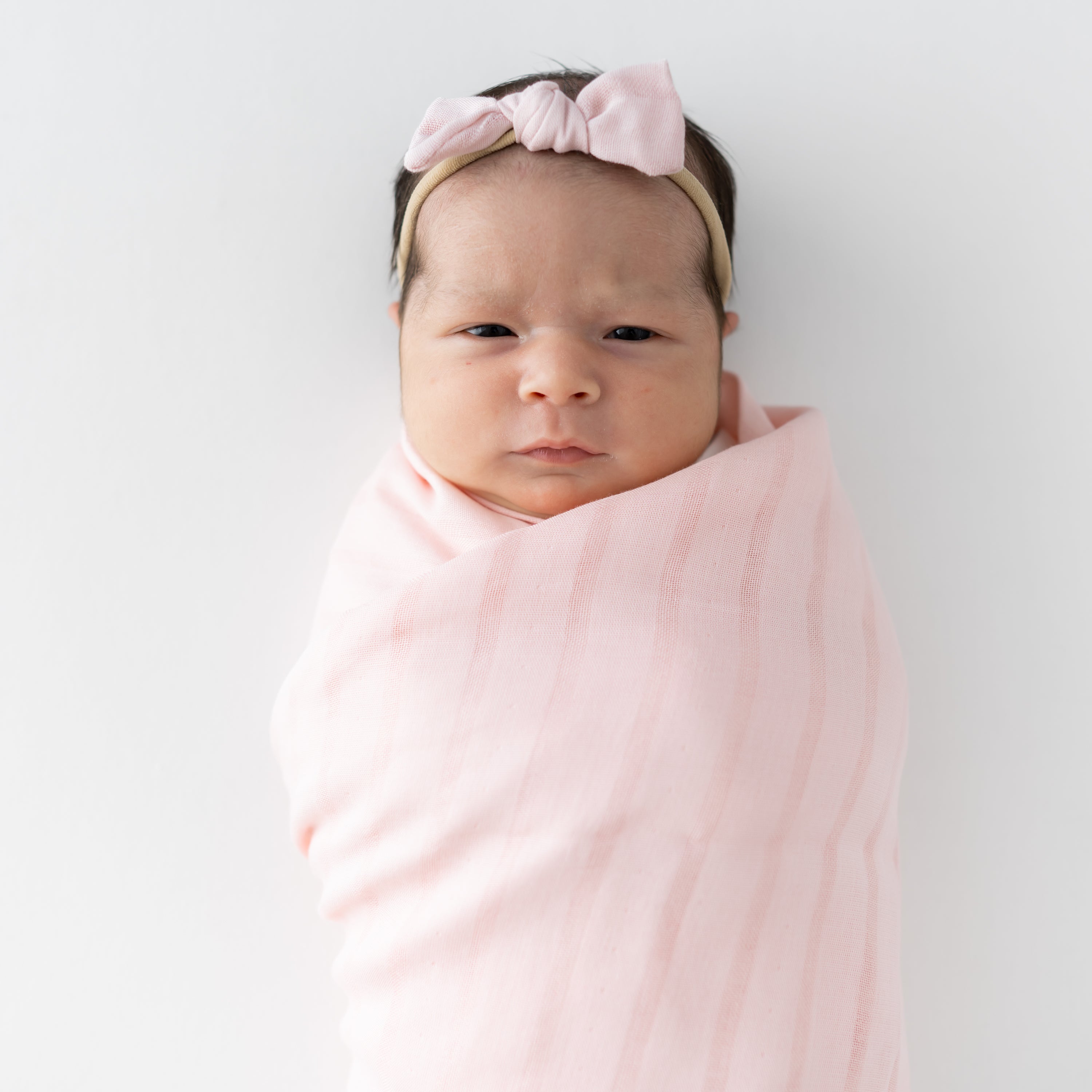 Newborn wrapped in a Swaddle Blanket in Blush and matching Tiny Muslin Bow