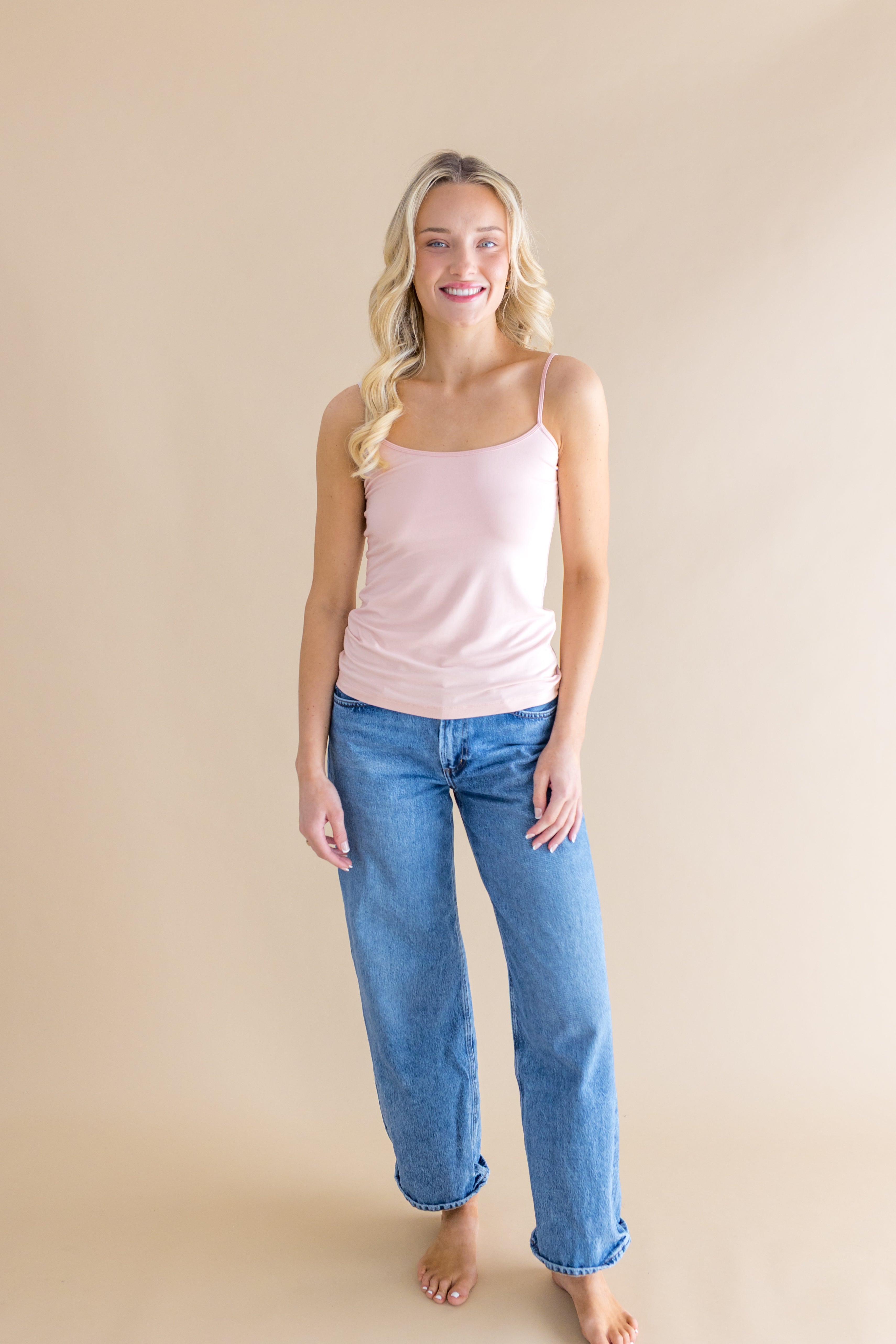 Woman wearing a pink tank top and blue jeans against a beige background