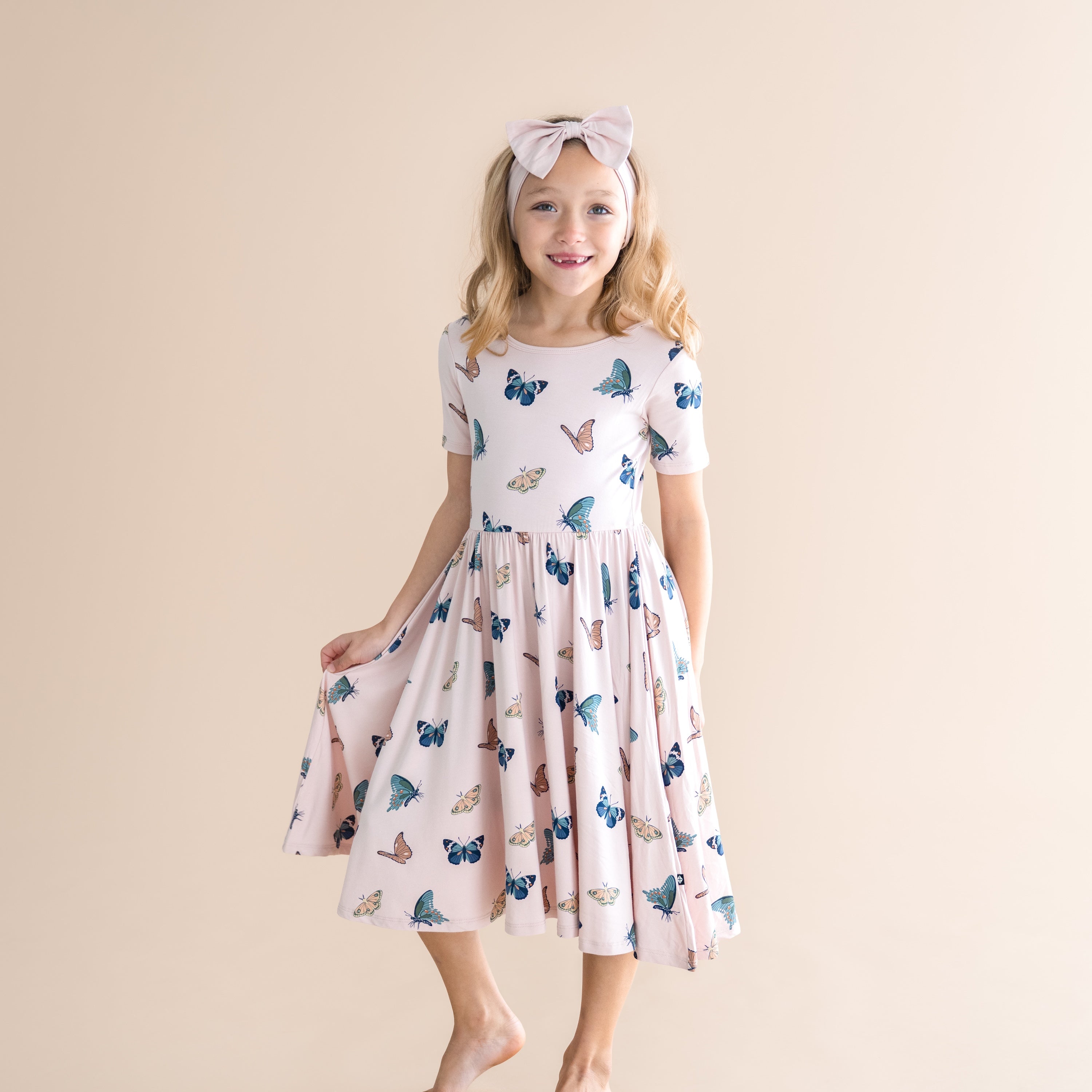 Young girl wearing a dress with butterfly pattern on a beige background