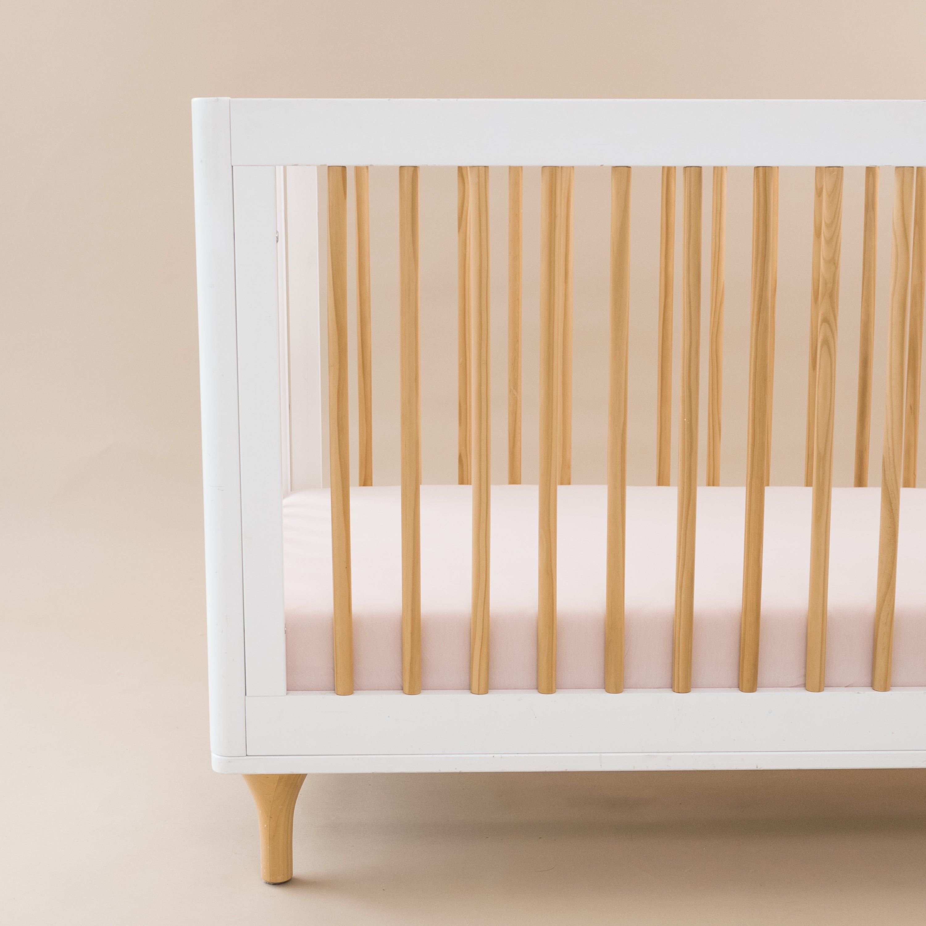 Crib Sheet in Blush shown on a mattress in a modern white and wooden crib