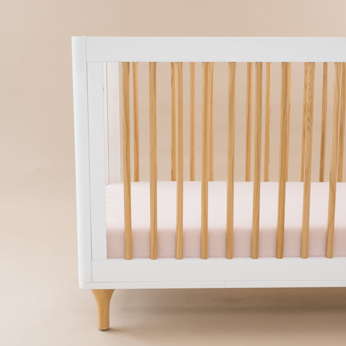 Crib Sheet in Blush shown on a mattress in a modern white and wooden crib