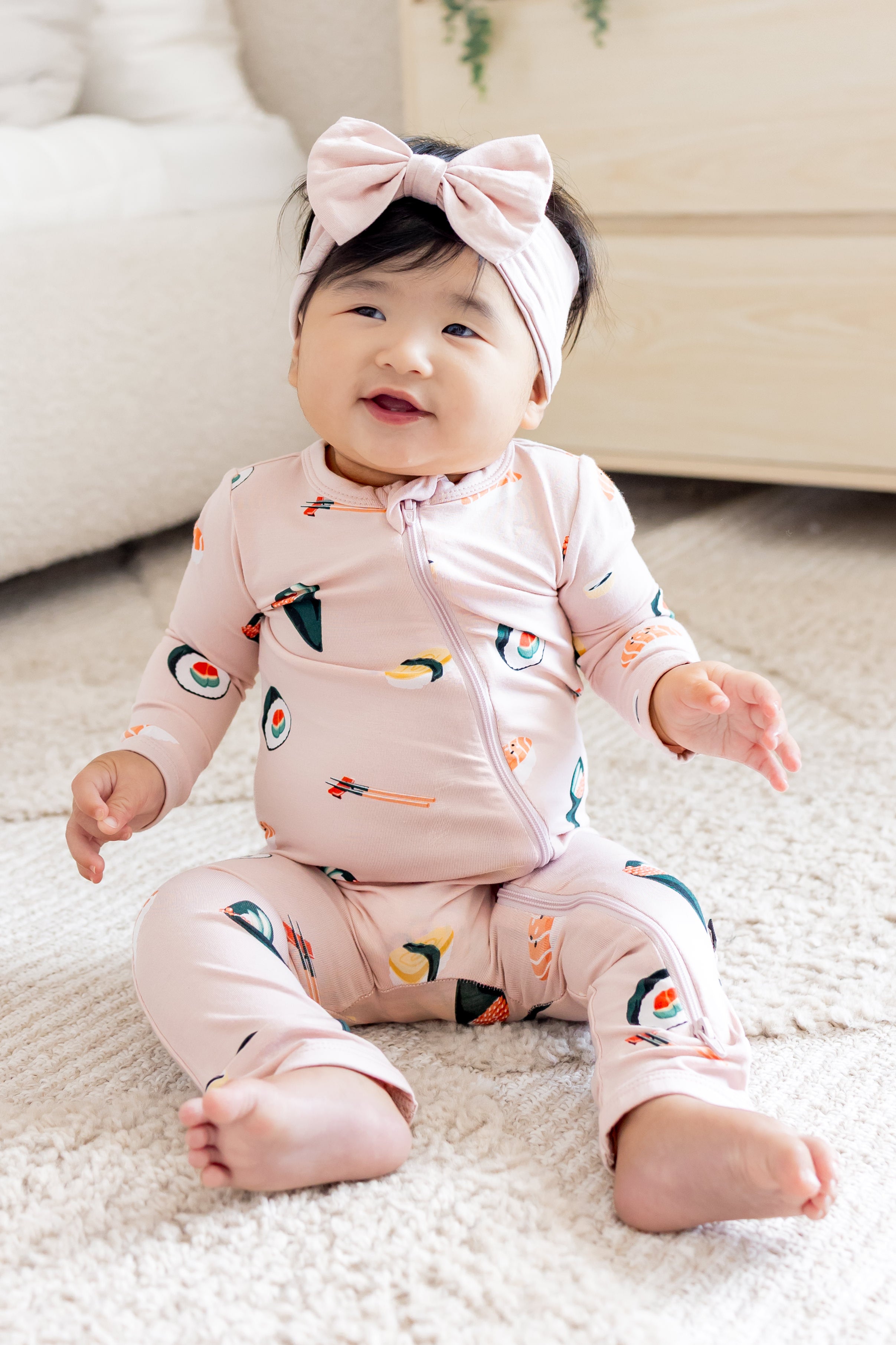 Baby sitting up soft smiling in blush sushi zipper romper and pink bow