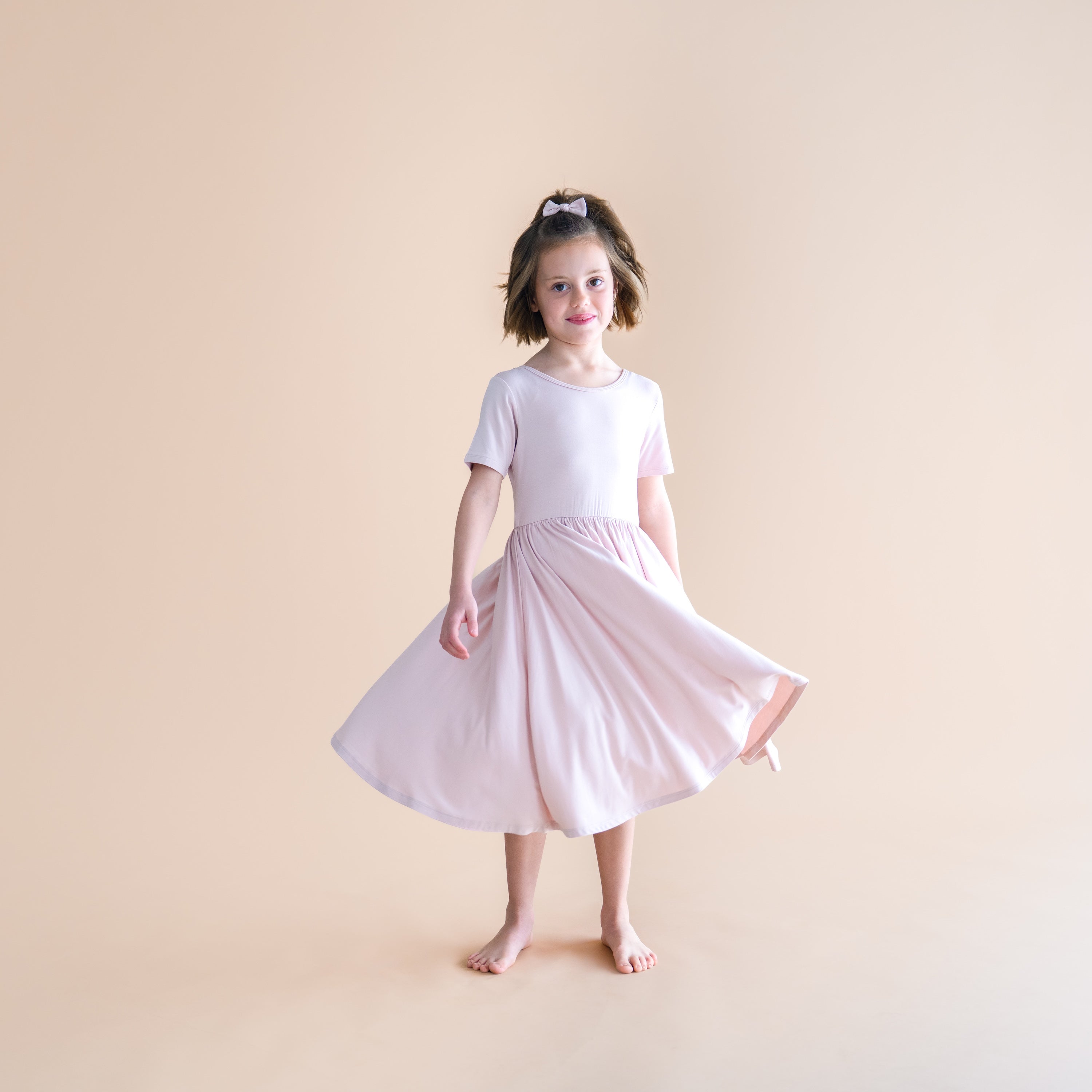 Young girl wearing a blush pink twirl dress on a beige background