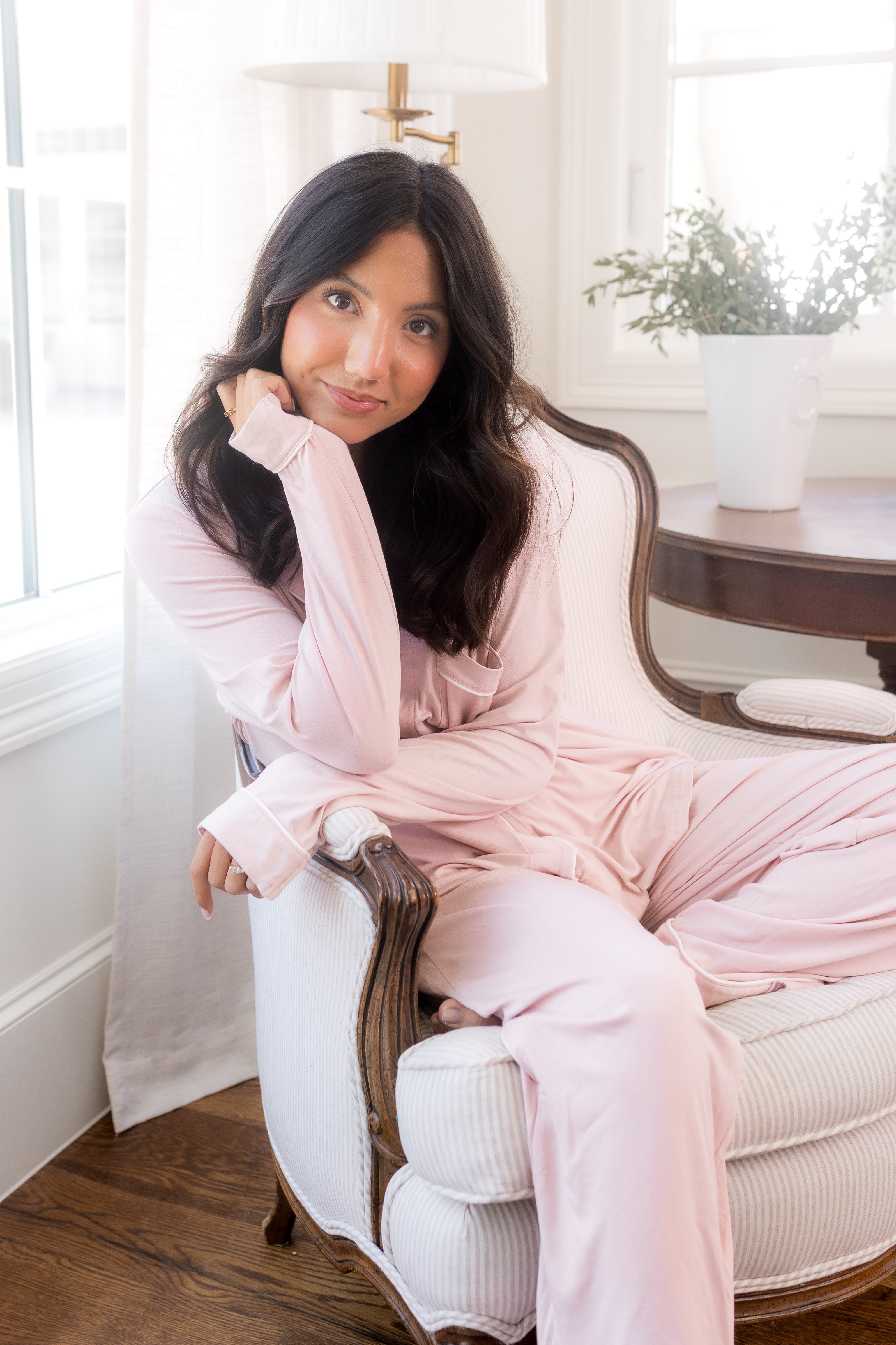 Smiling female sitting in a chair wearing light pink pajamas with a white trim