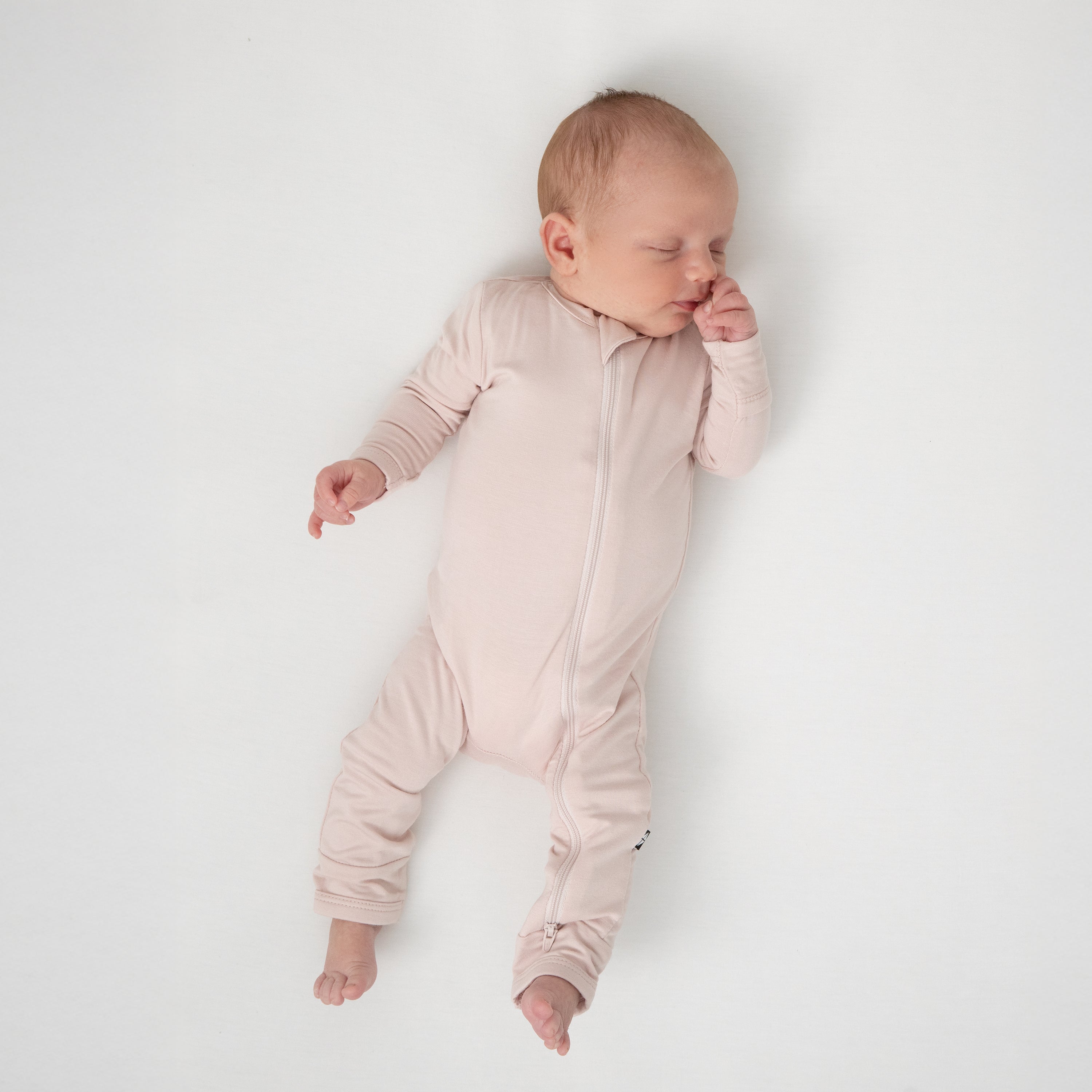 Sleeping newborn laying on a white blanket wearing the Zippered Romper in Blush