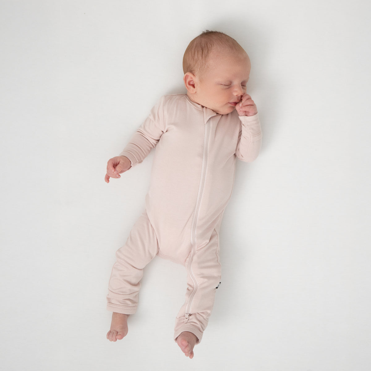 Sleeping newborn laying on a white blanket wearing the Zippered Romper in Blush