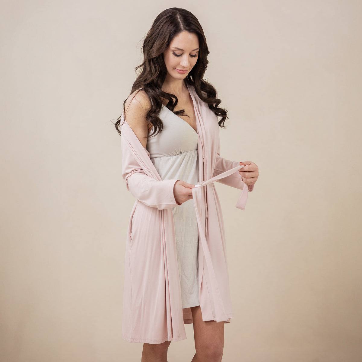 Female model wearing the Women's Lounge Robe in Blush with one shoulder mid arm while holding the waist tie in her hands