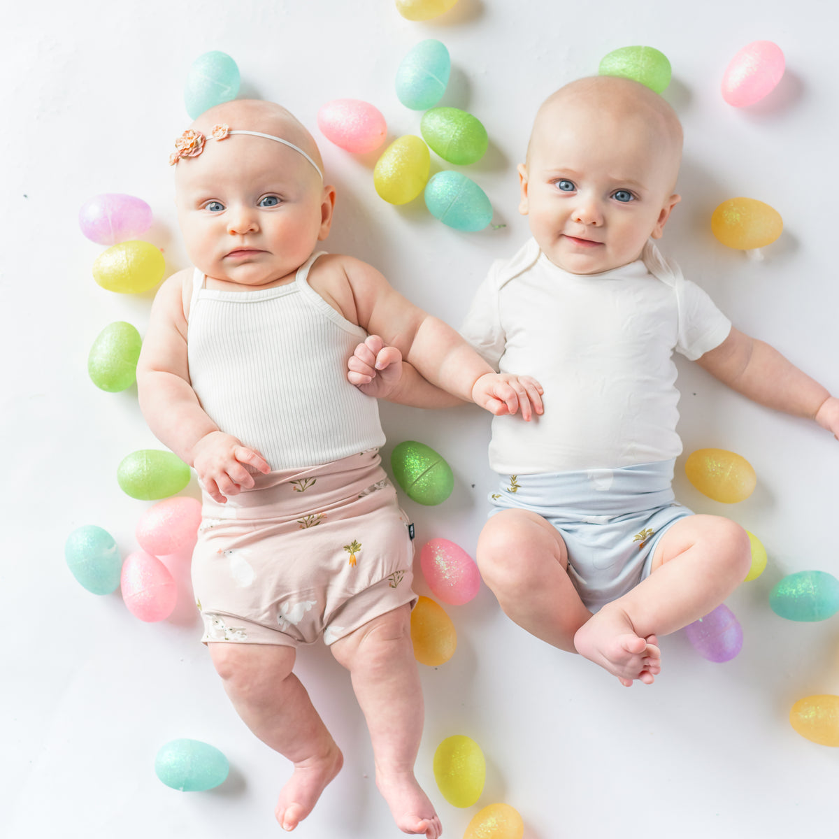 Two babies in Bummies in Blush and Ice Rabbit surrounded by easter eggs