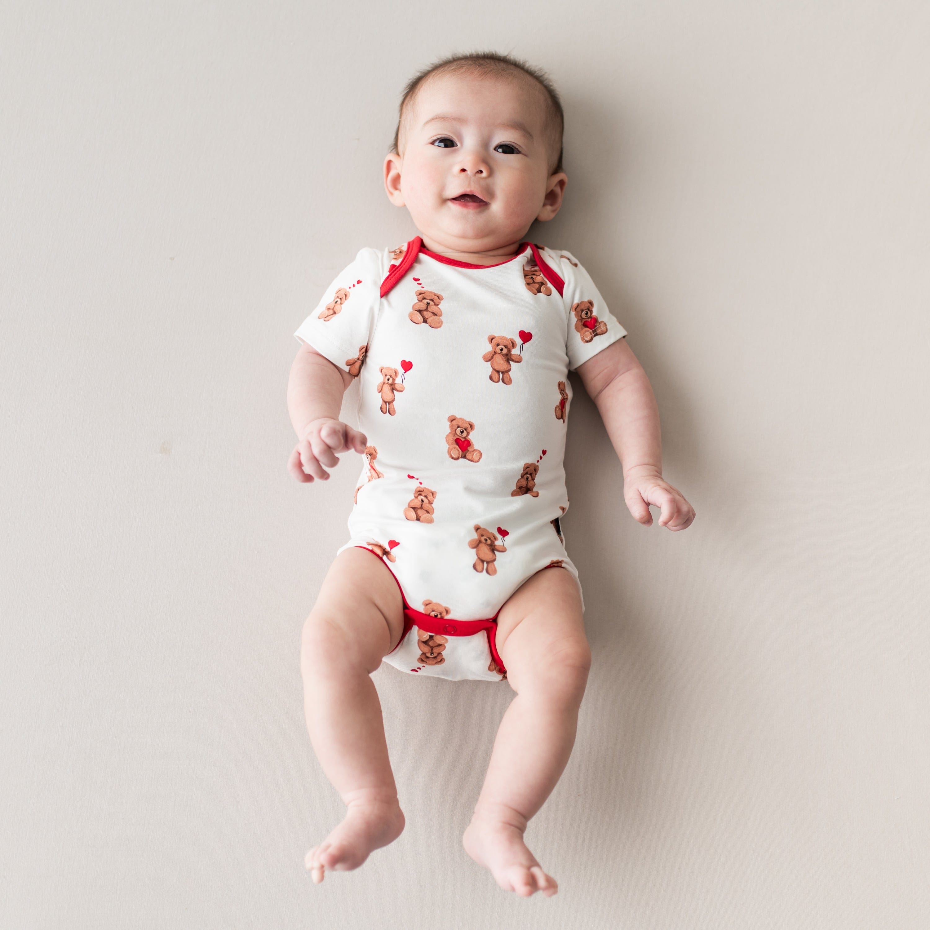 Infant laying on a light neutral surface wearing the soft and stretchy Bodysuit in Bear Hearts
