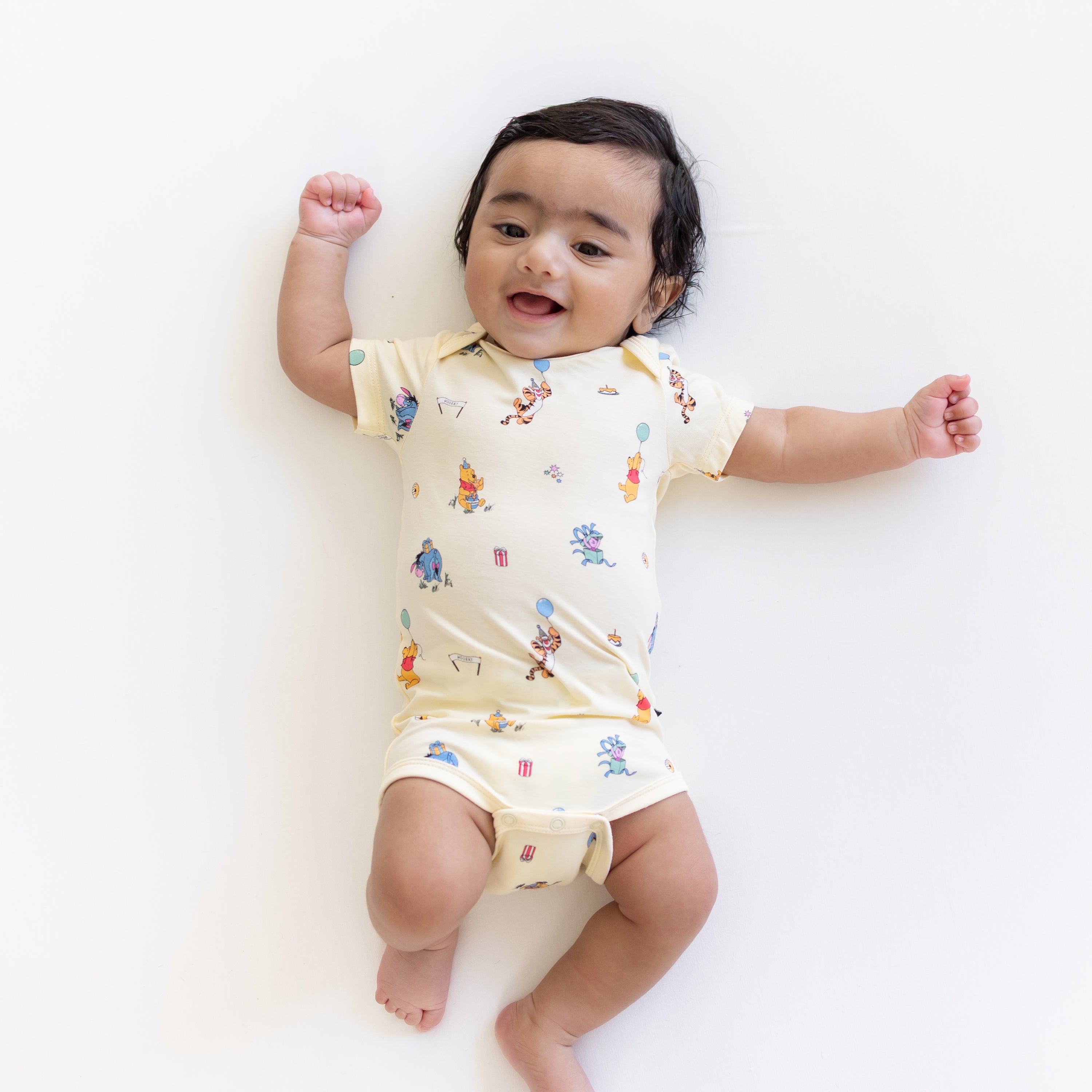 Infant laying on a light neutral surface wearing the Bodysuit in Winnie the Pooh Celebration