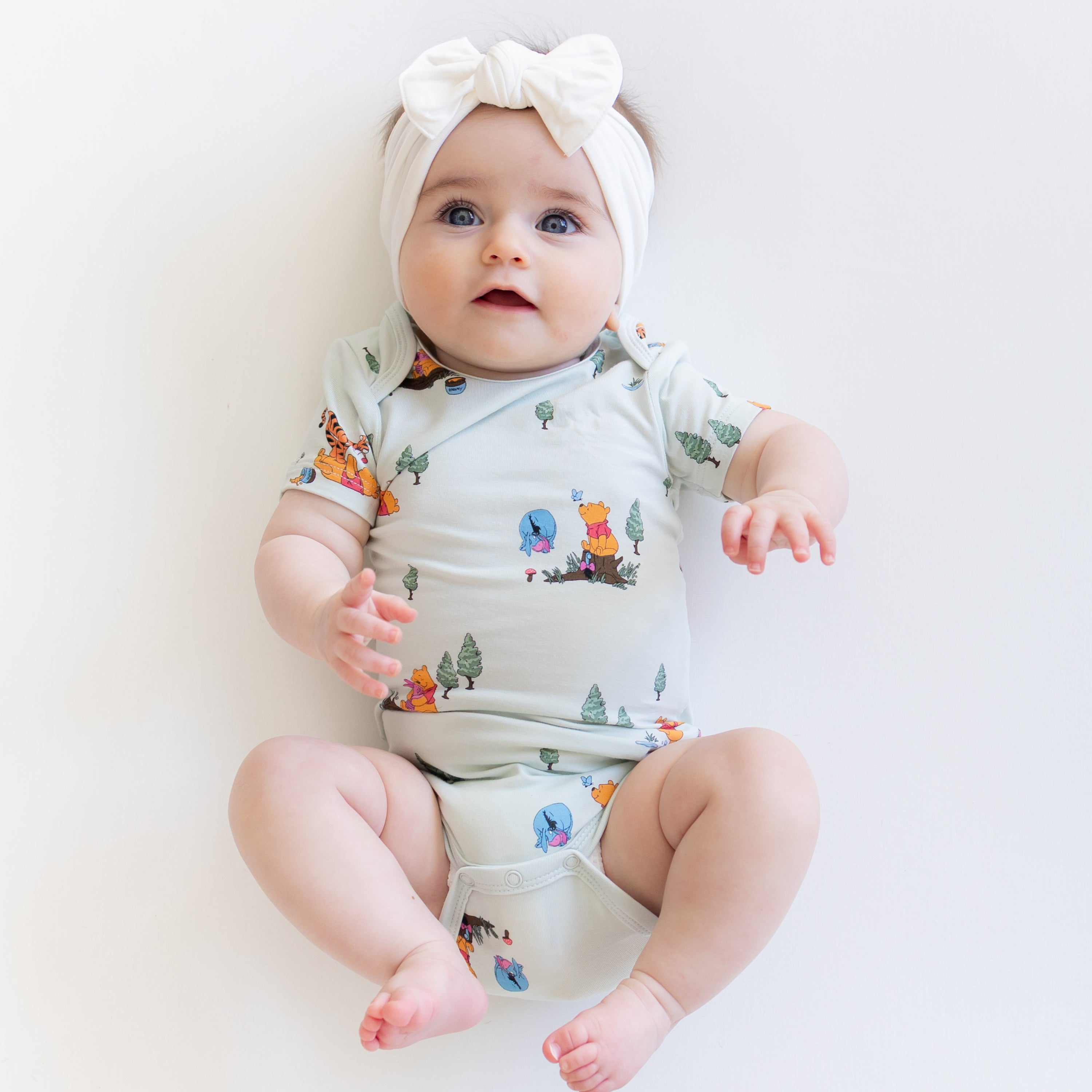 Close up of infant wearing the Bodysuit in Winnie the Pooh Hundred Acre Wood with a white bow