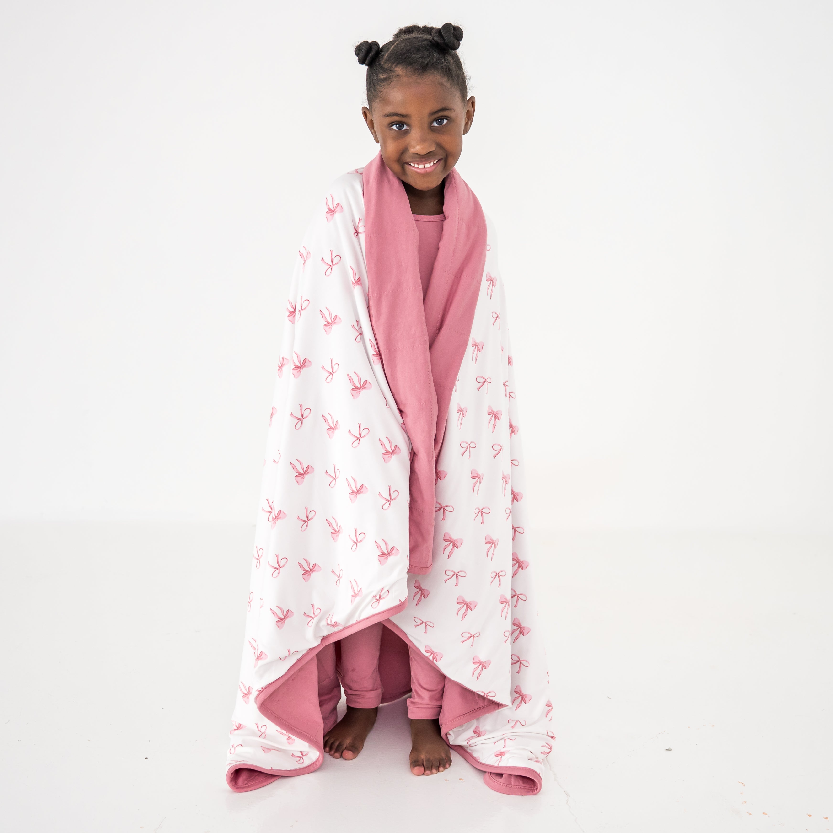 Toddler wrapped in a blanket that has a pink bow pattern on a white background with pink trim