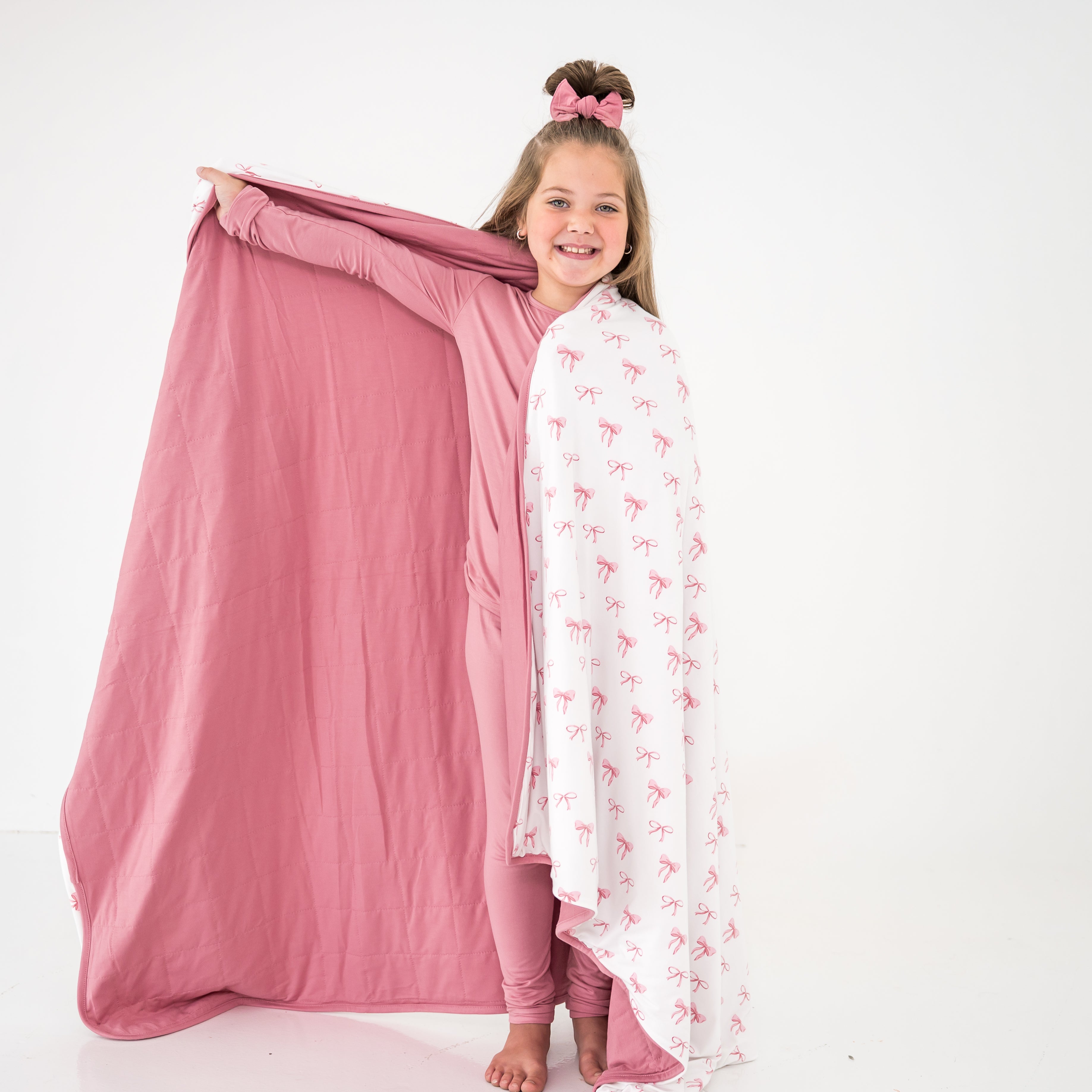 Girl holding a pink and white blanket with pink bow patterns on a white background