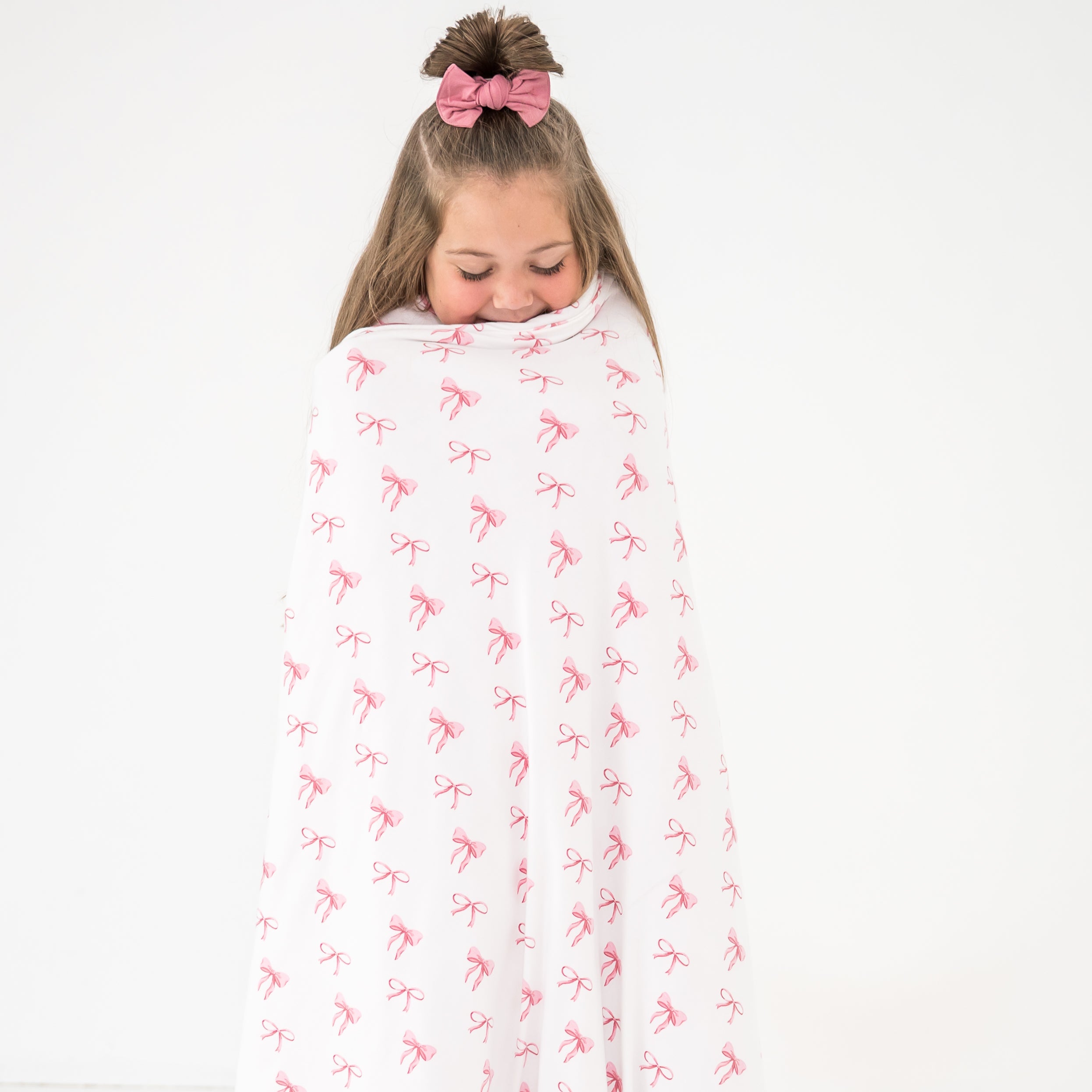Child wrapped in a pink and white bow patterned blanket on a white background