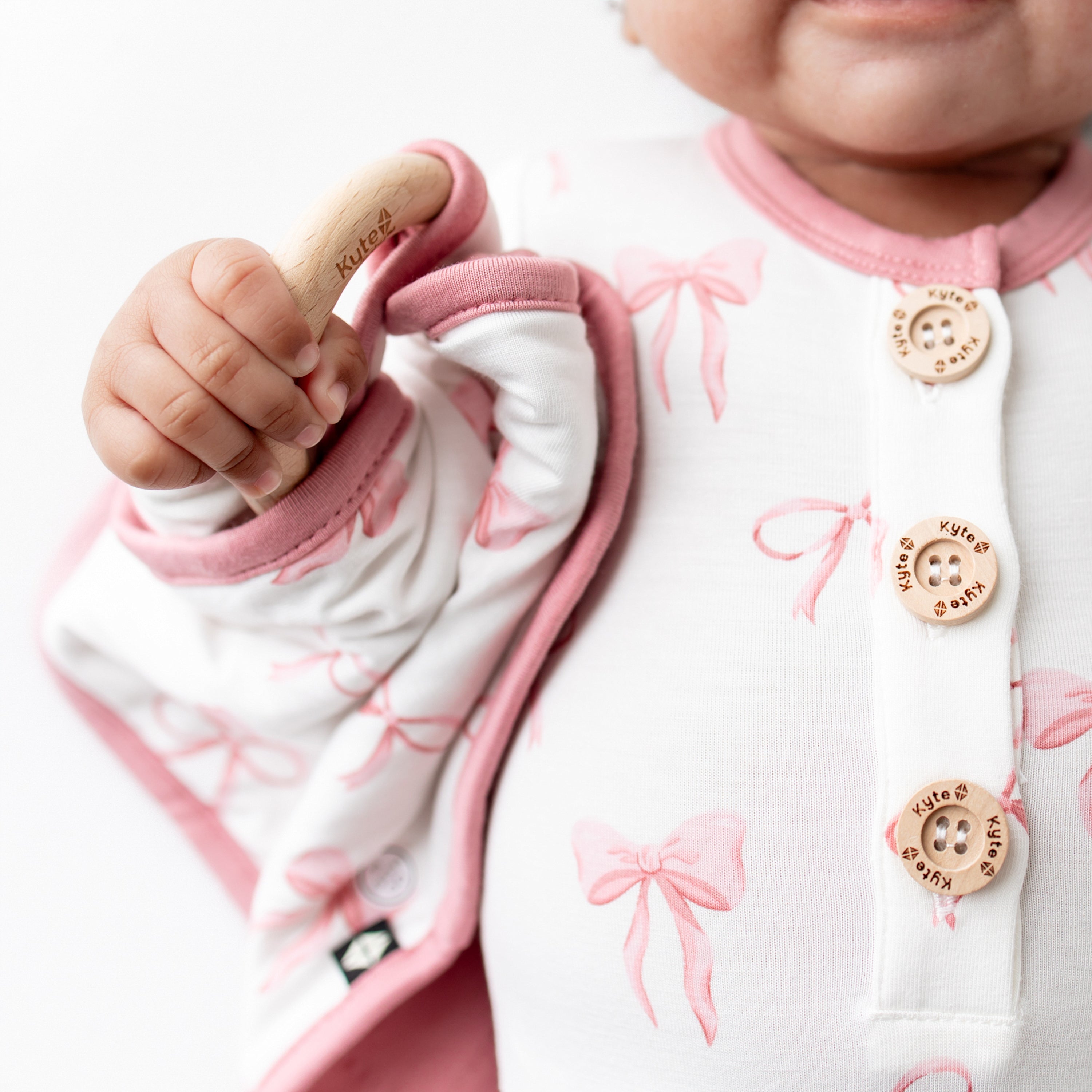 Infant holding the Lovey in Bow with Removable Wooden Teething Ring in matching knotted gown