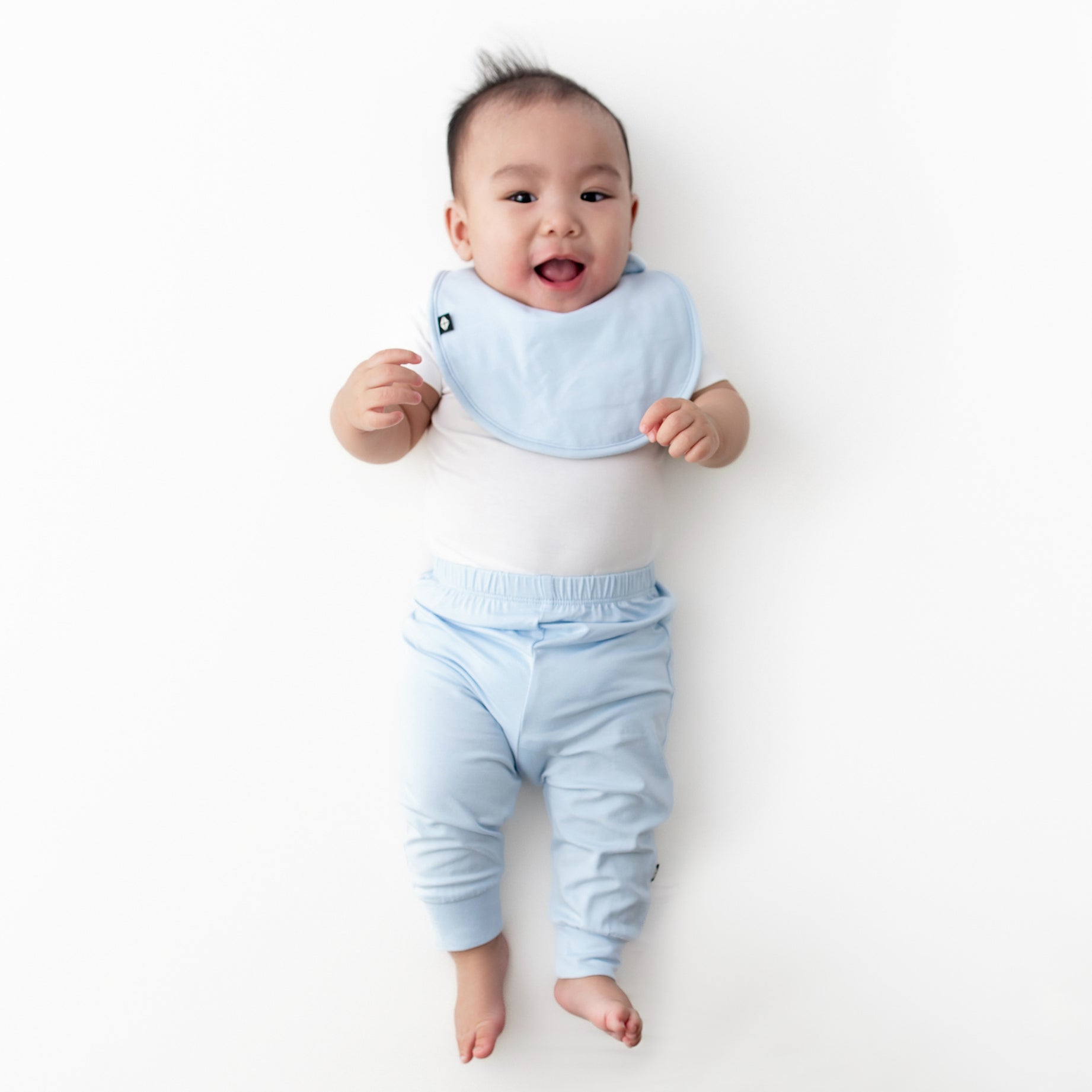 Infant wearing the Cushy Bib in Breeze blue with a white short sleeve bodysuit and matching blue pants
