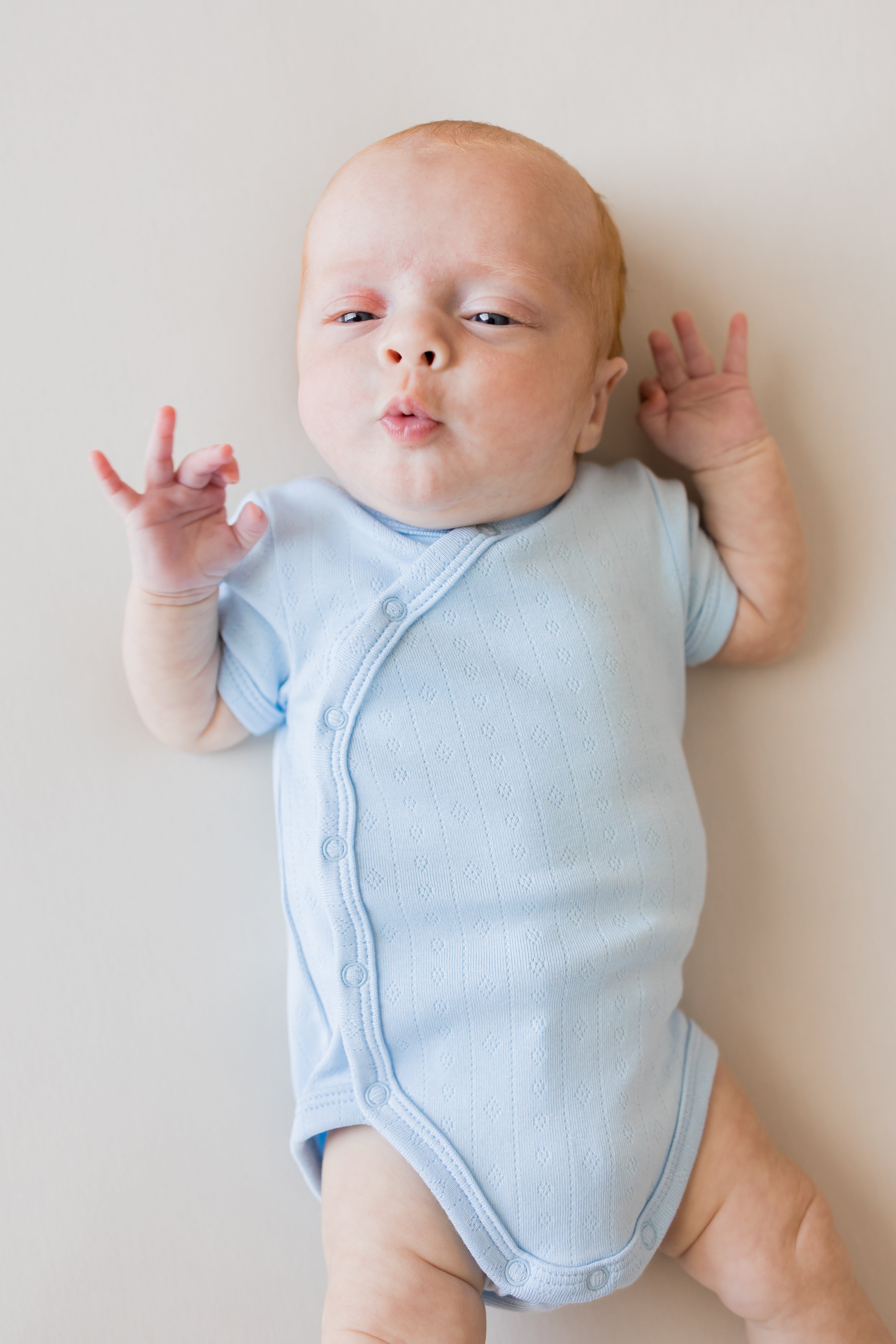 Close up of Baby wearing Pointelle Kimono Bodysuit in Breeze color on a beige background