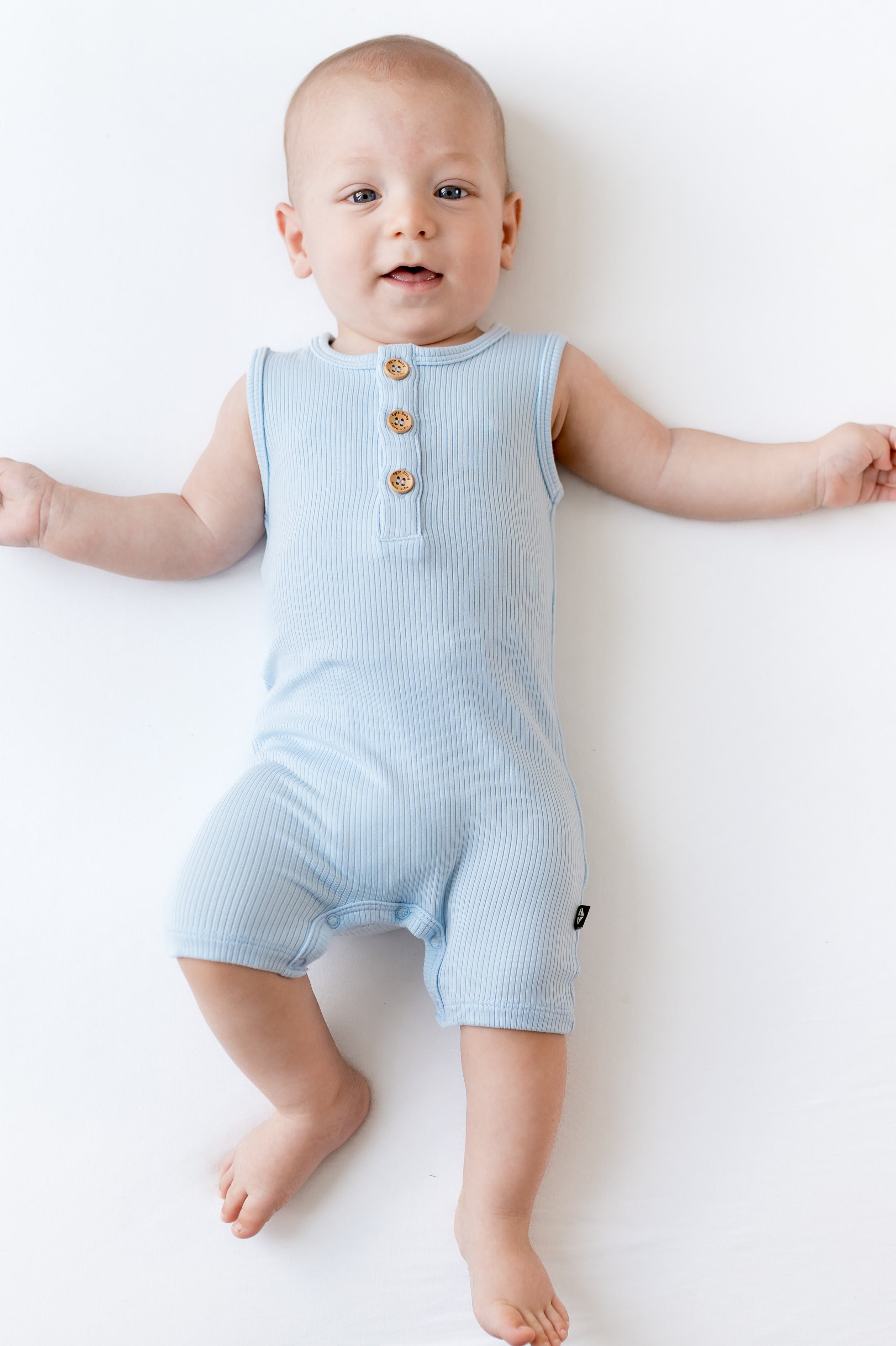 Infant laying on a white surface wearing the Ribbed Sleeveless Shortall in Breeze