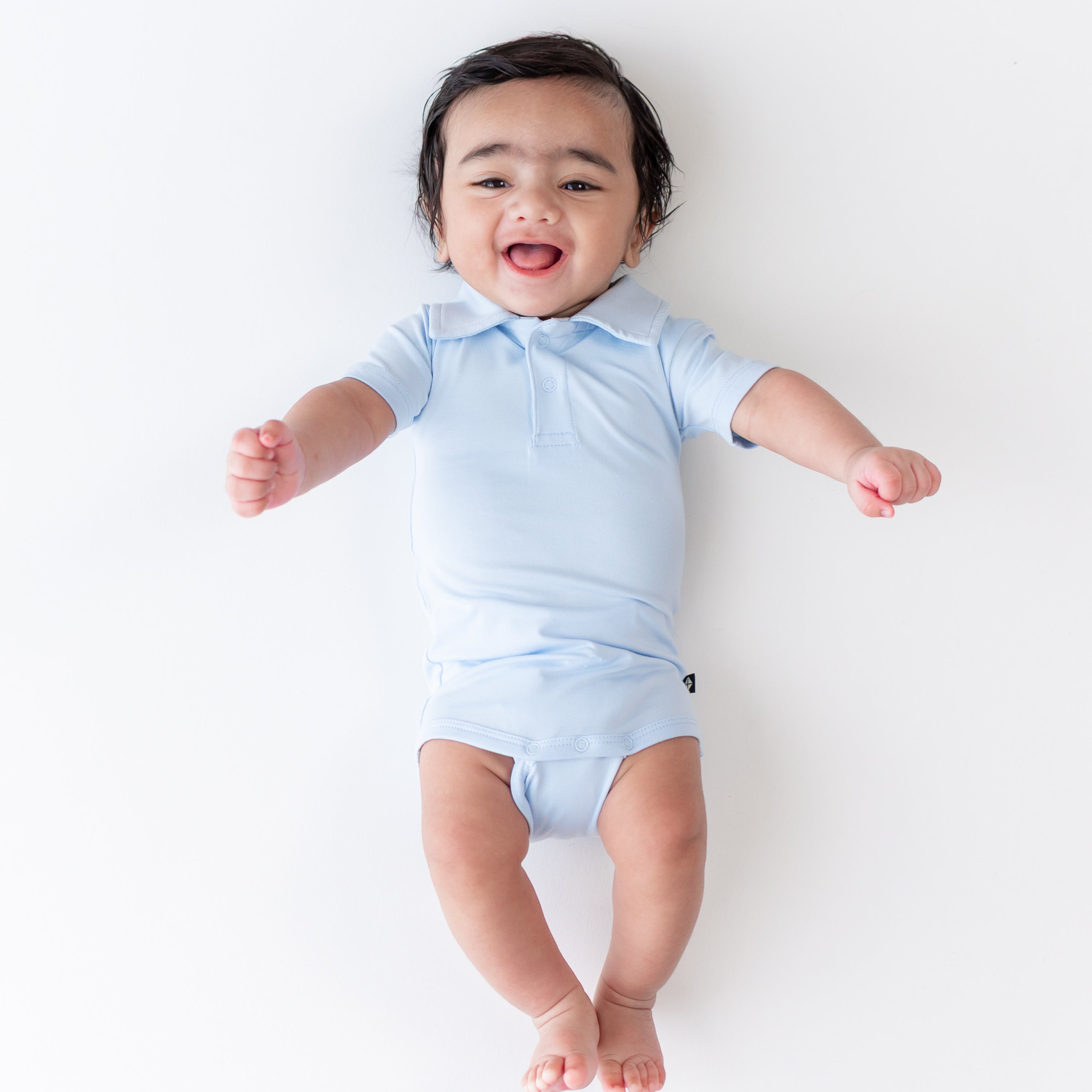 Smiling infant wearing the Polo Bodysuit in Breeze on a light neutral background