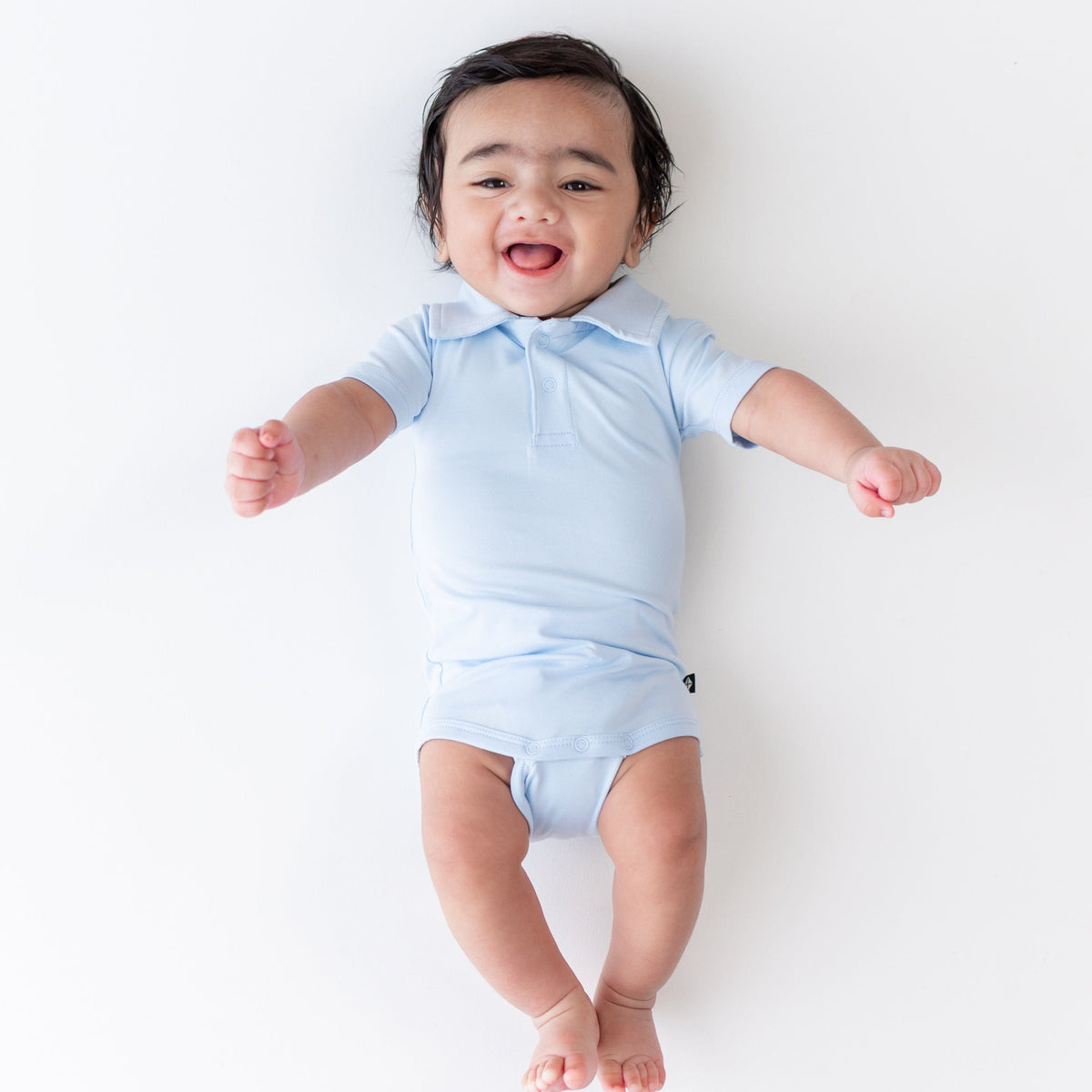 Smiling infant wearing the Polo Bodysuit in Breeze on a light neutral background