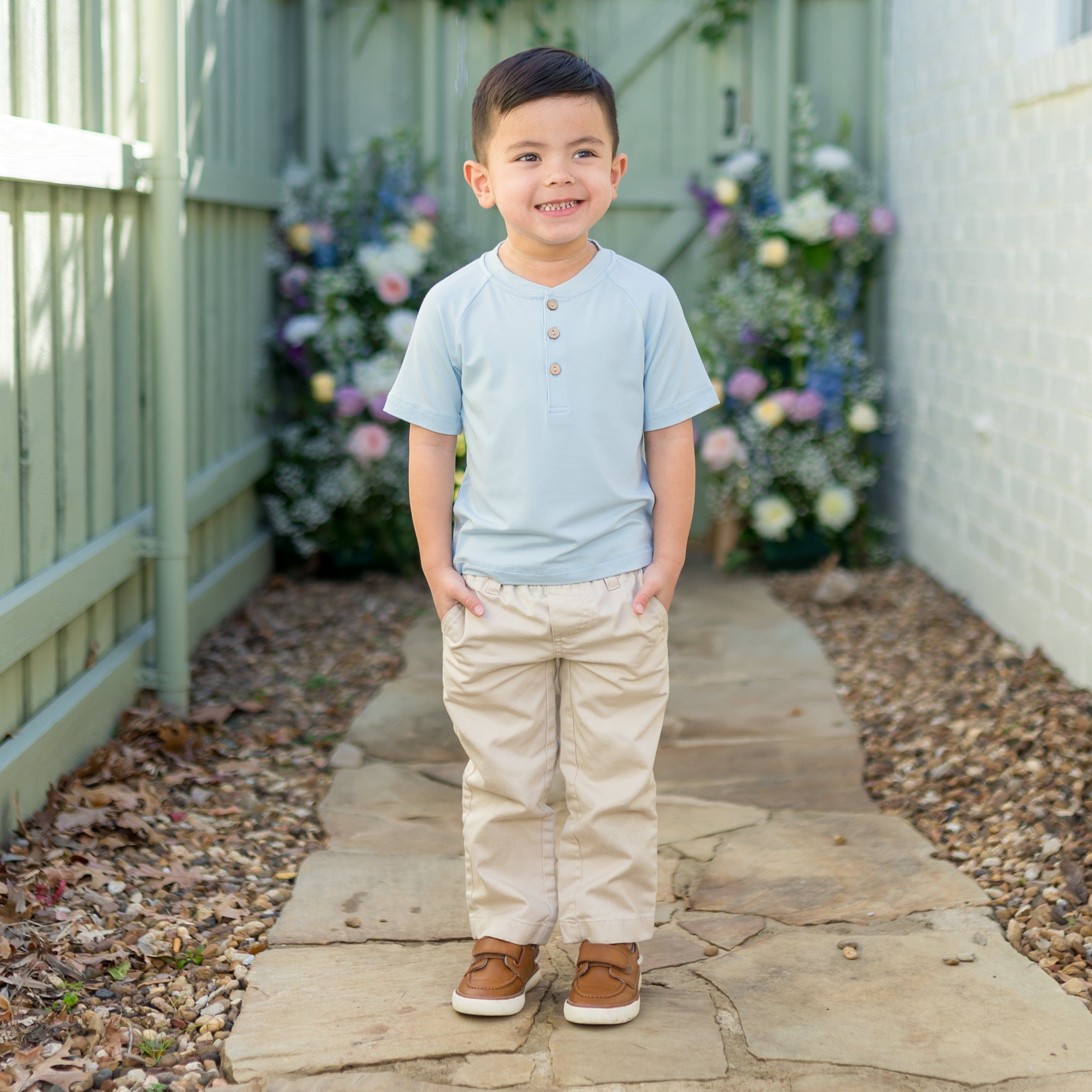 Young boy wearing the Short Sleeve Toddler Henley Tee in Breeze with kakhi colored pants standing on a path