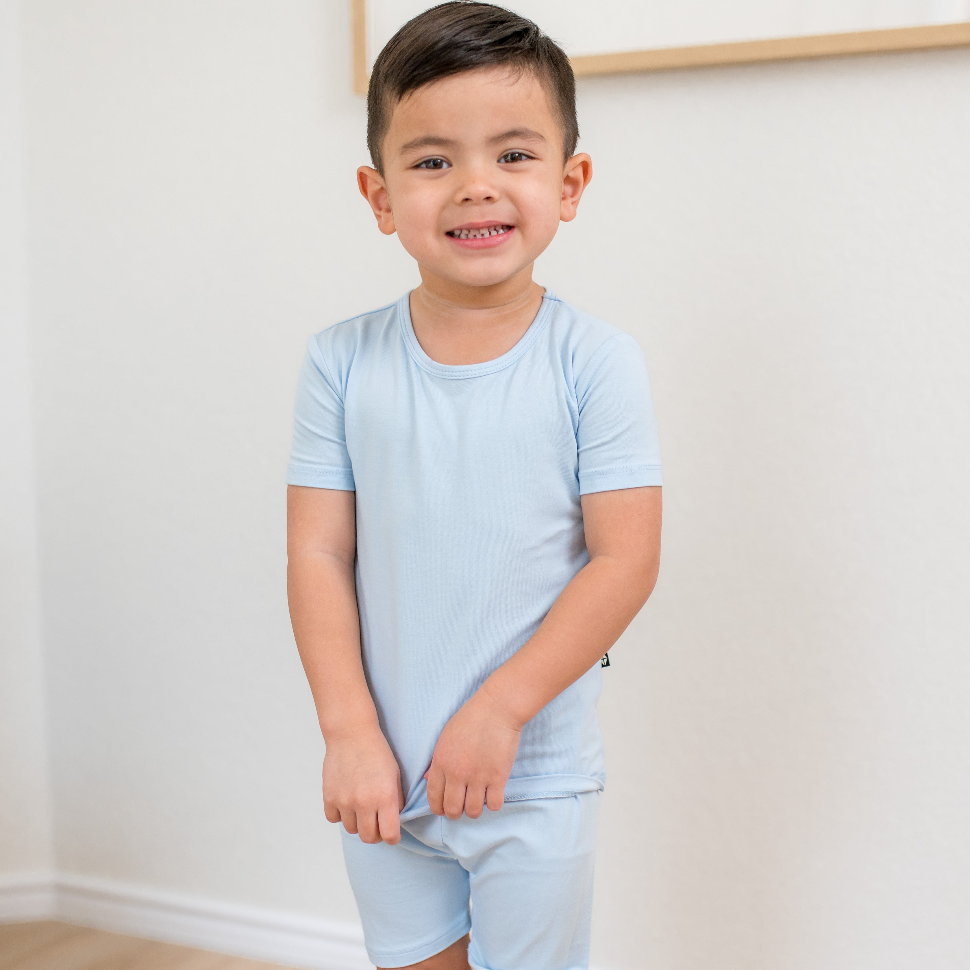 Young boy standing in front of a white wall wearing the Short Sleeve Pajamas in Breeze