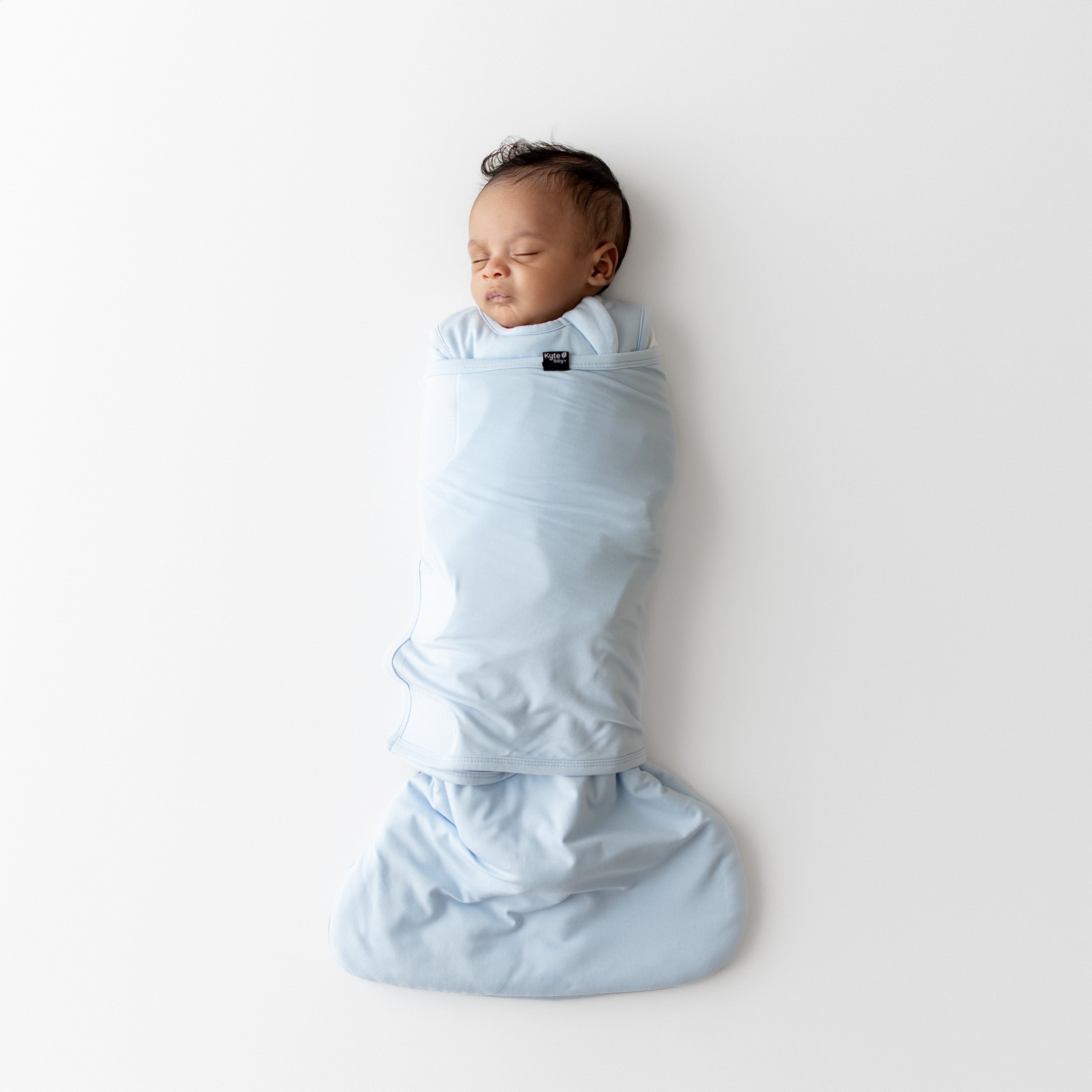 Baby swaddled in a kyte baby sleep bag swaddler in a light blue color