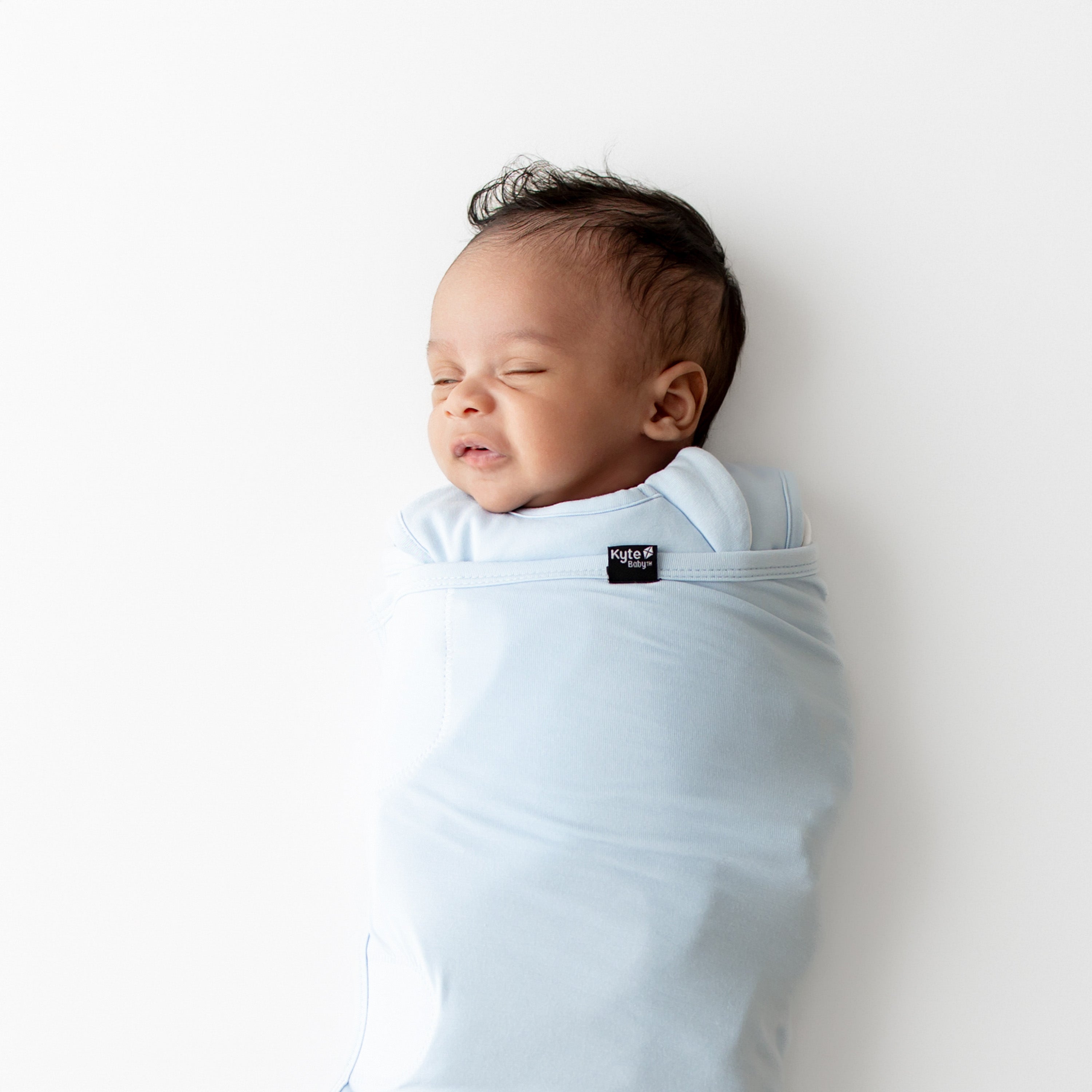 Newborn baby swaddled in a light blue swaddler on a white background