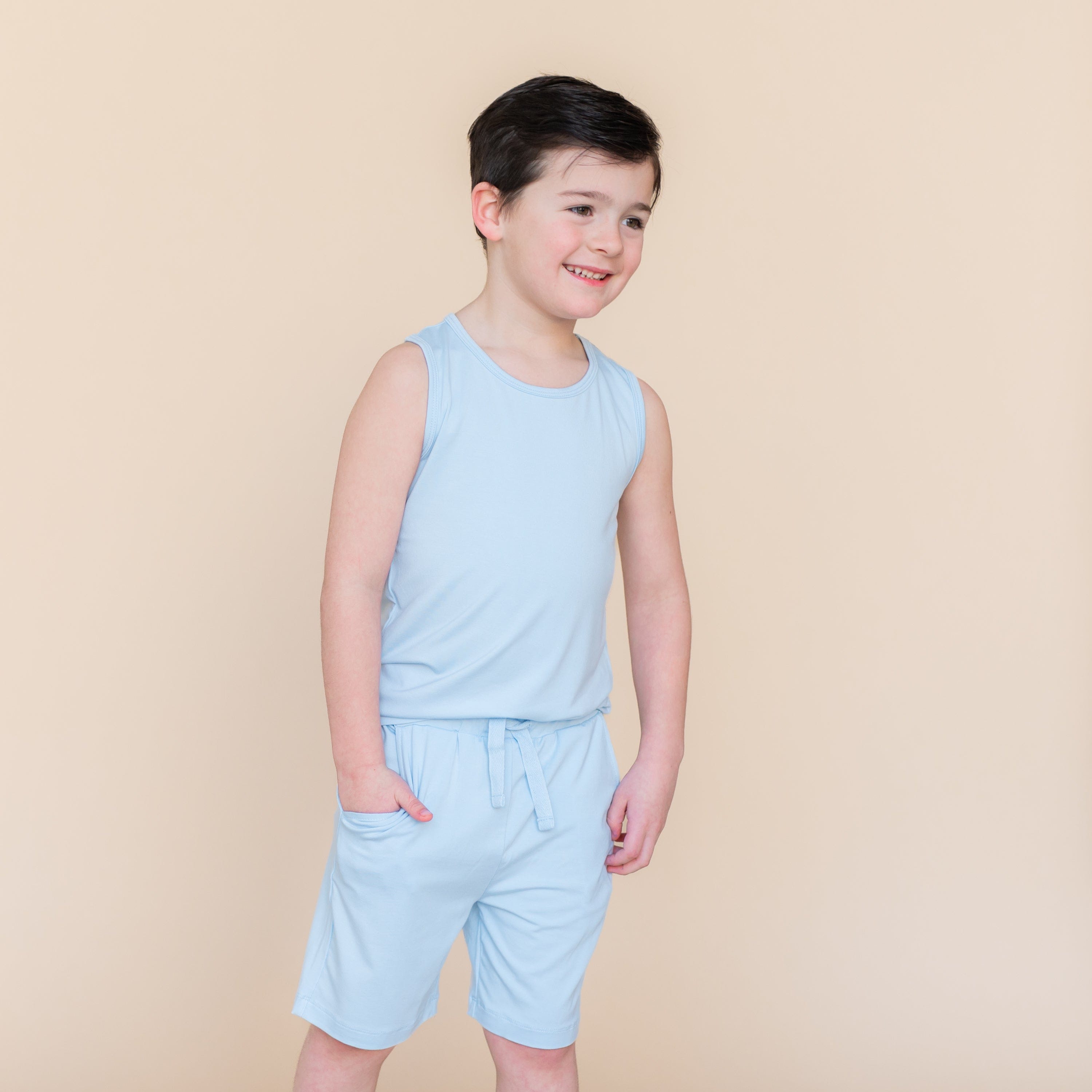 Smiling boy standing with one hand in the pocket of the Drawstring Short in Breeze paired with a matching tank top