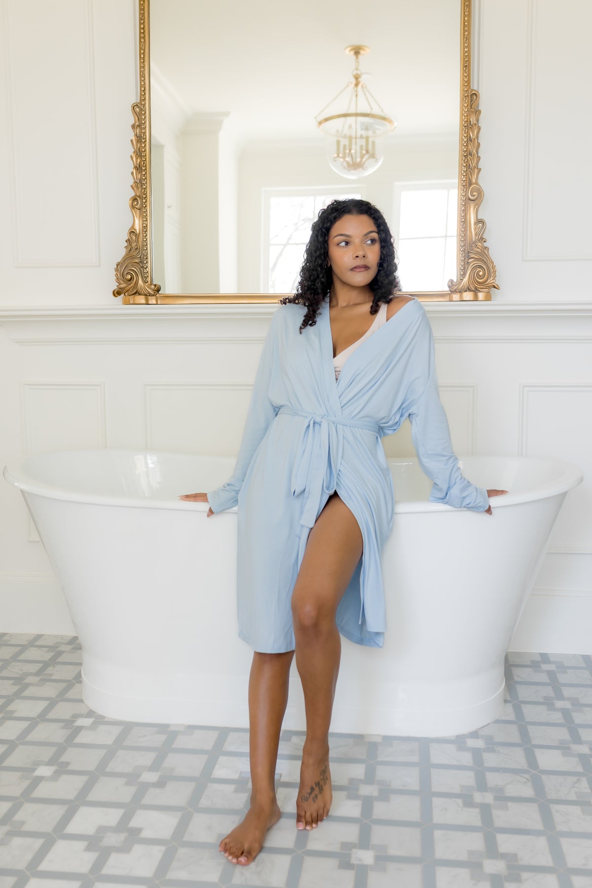 Female modeling the Women's Lounge Robe in Breeze leaning against a white bath tub