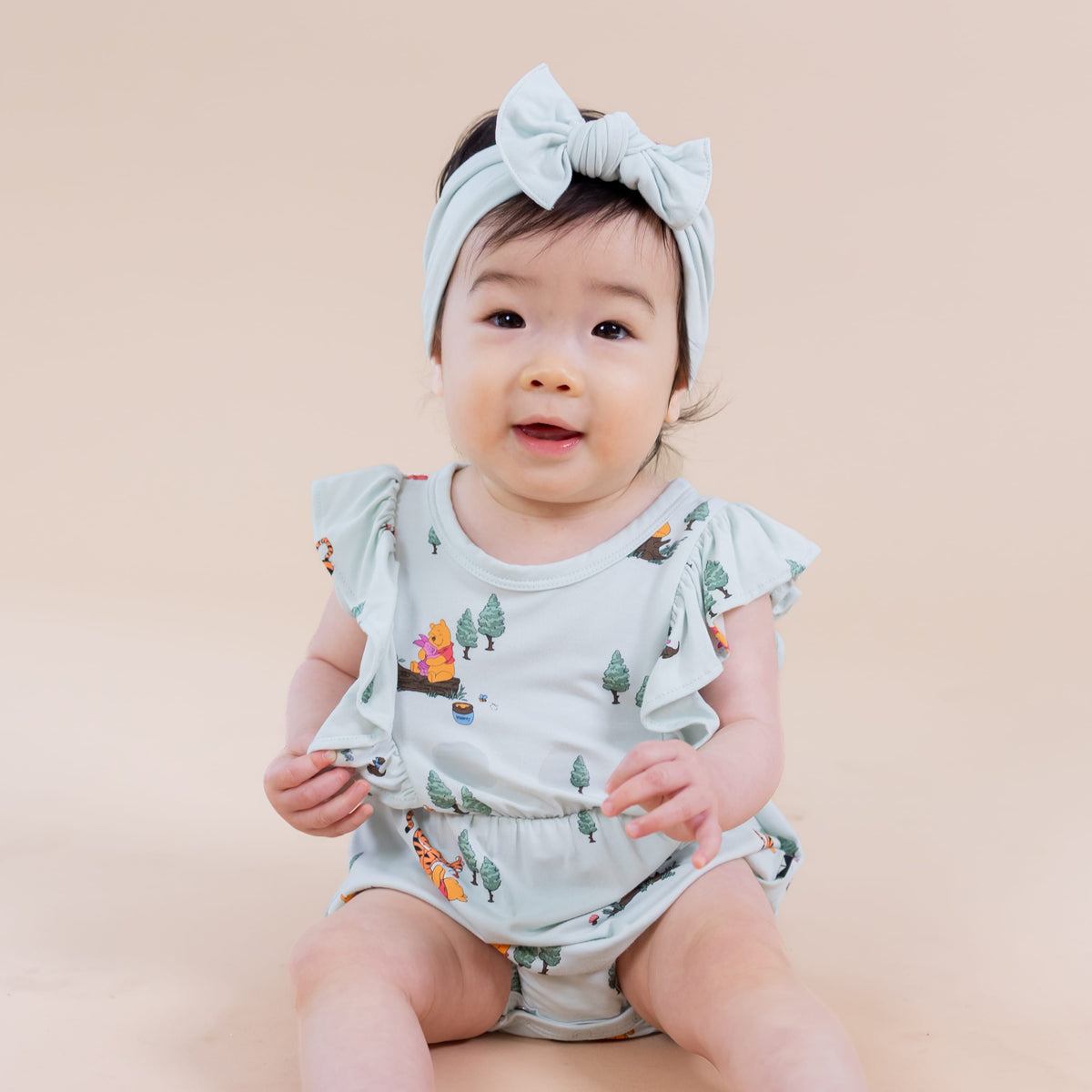 Close up of an infant wearing the Bubble Romper in Winnie the Pooh Hundred Acre Wood sitting on the floor